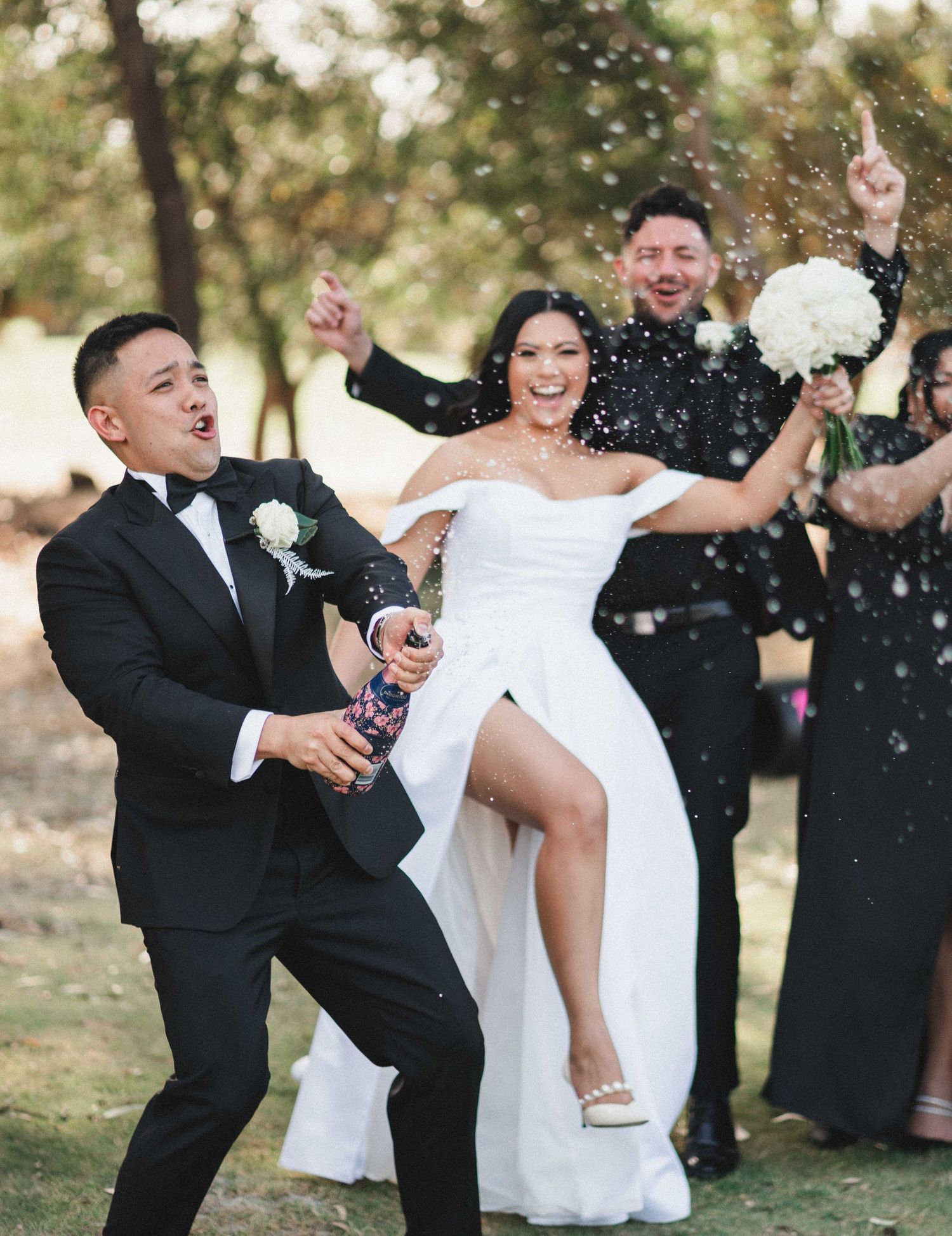 Wedding party celebrating with champagne spray and joyful expressions outdoors.