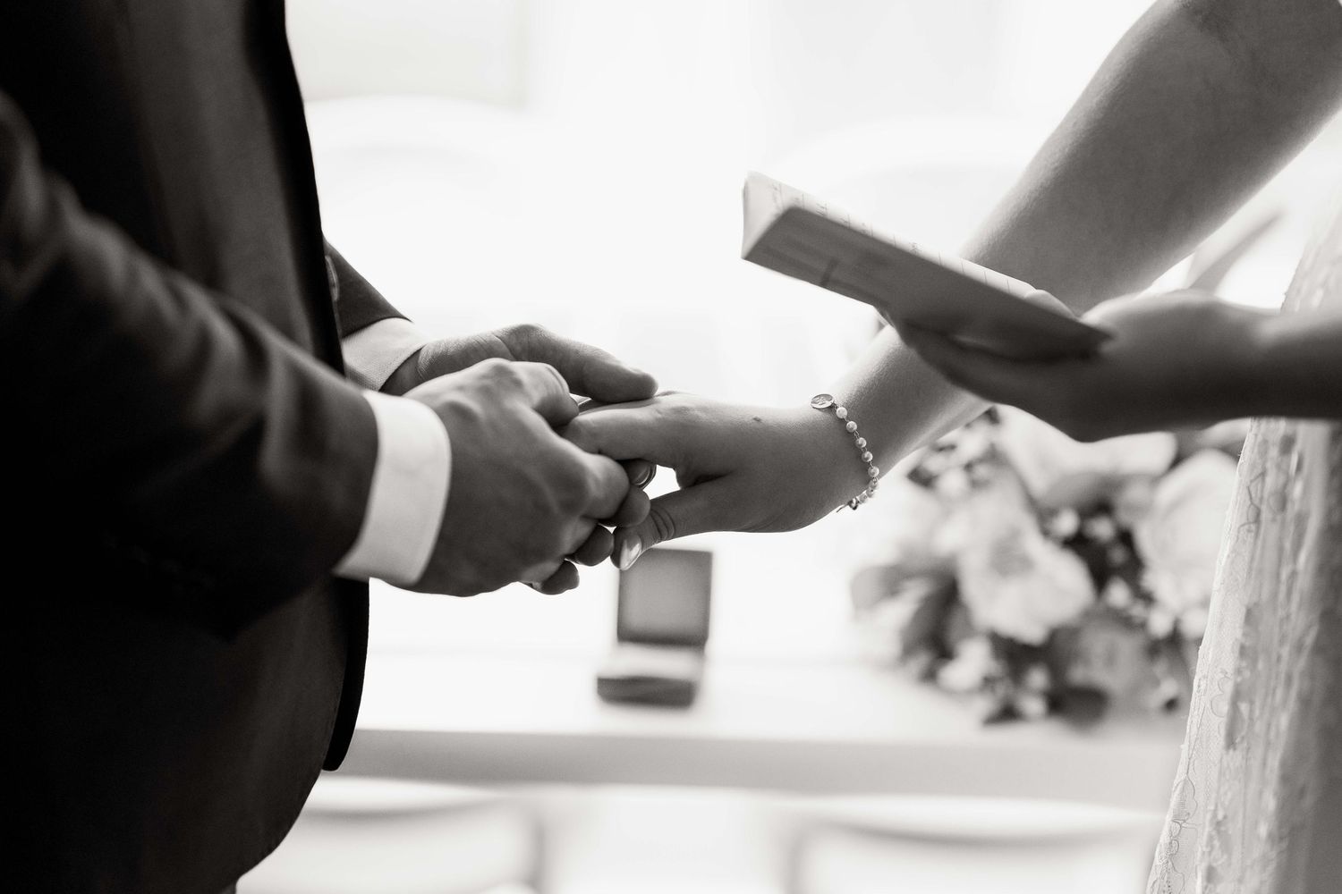 Close-up of wedding rings being exchanged during ceremony in black and white.