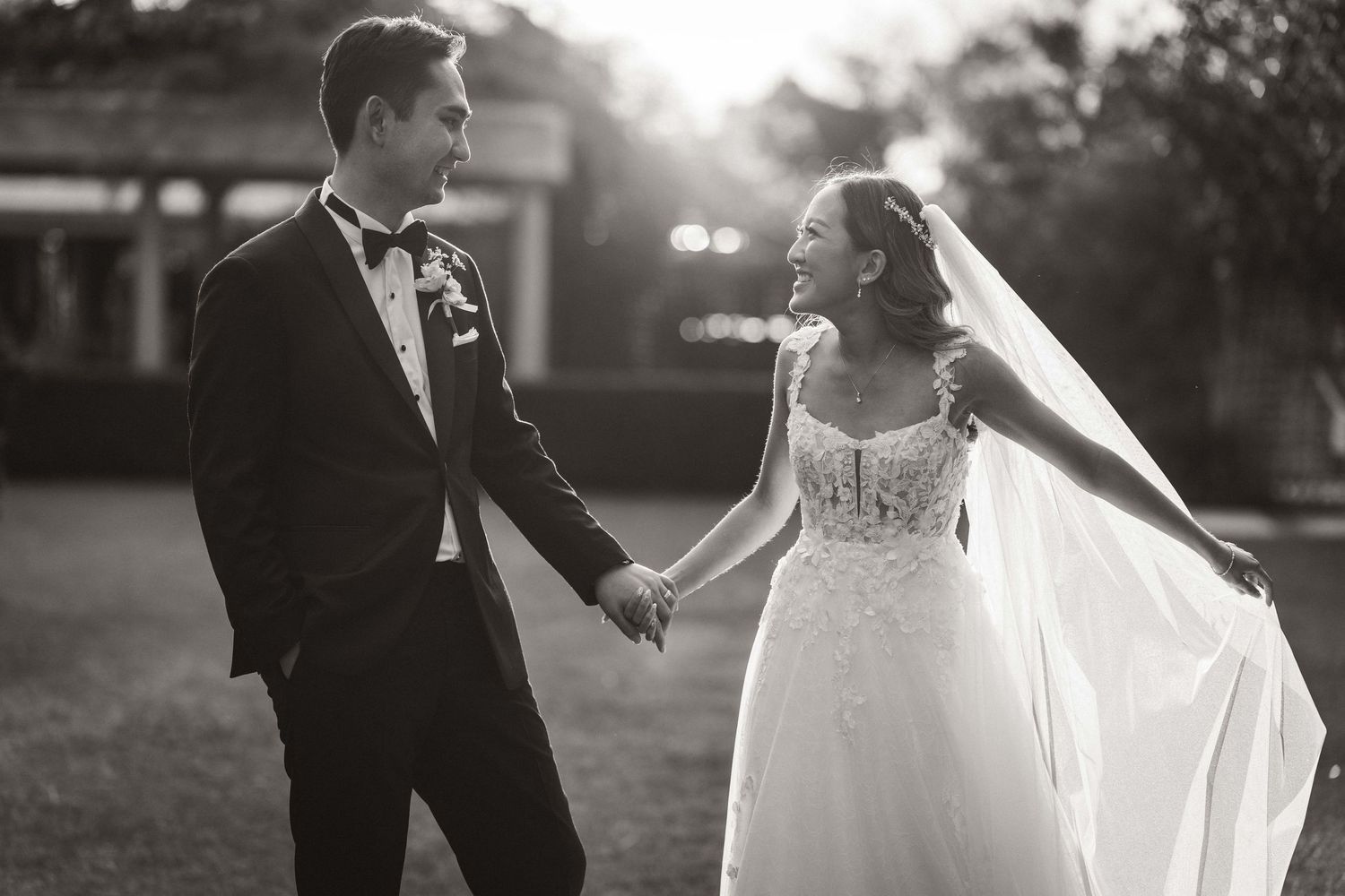Black and white sunset portrait of newlyweds with flowing veil in romantic outdoor setting.