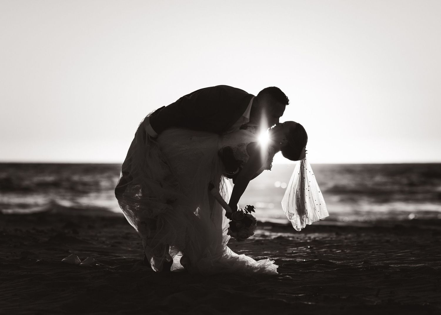 Black and white silhouettes of couple sharing intimate moment on beach at sunset.