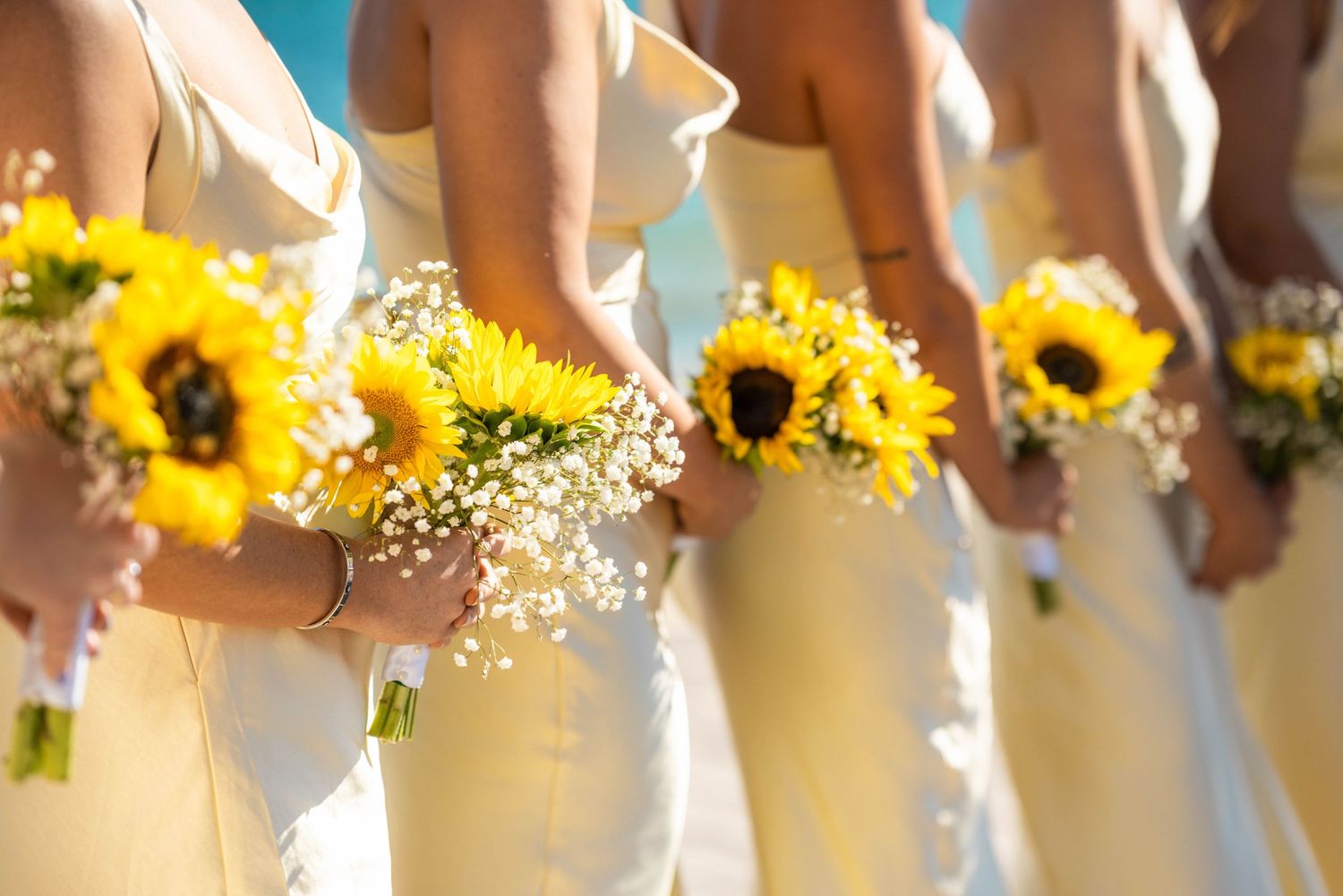 Row of bridesmaids holding bright yellow sunflower bouquets in light yellow dresses.