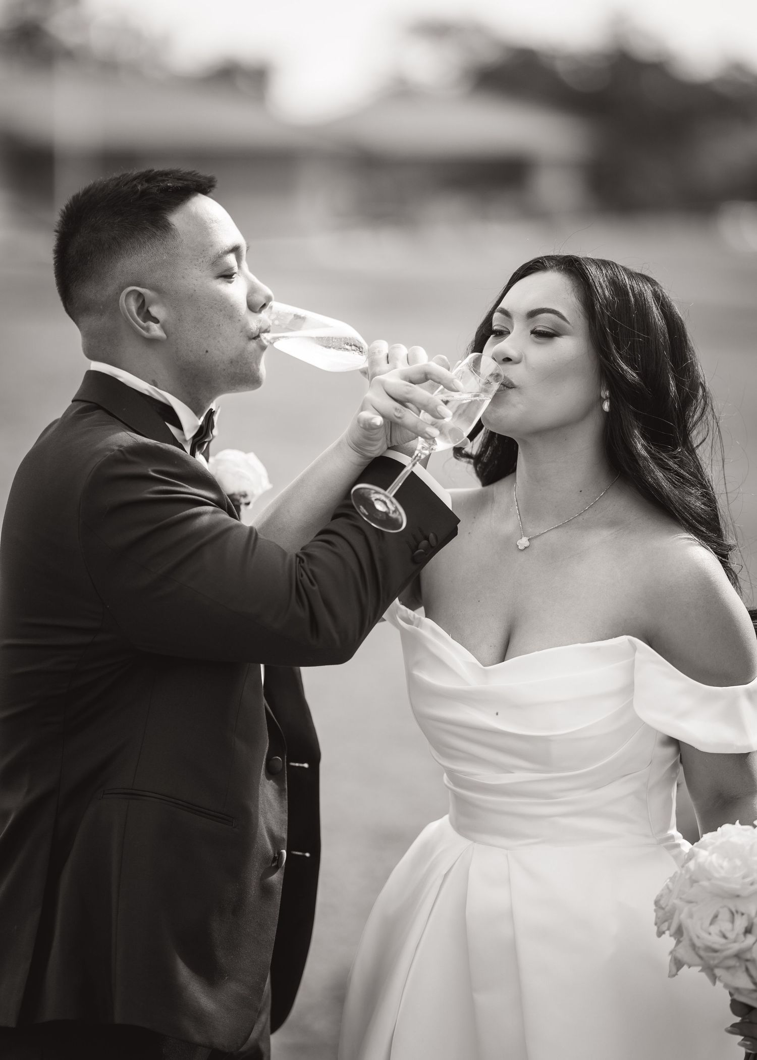 Black and white photo of newlyweds sharing a champagne toast in elegant wedding attire.