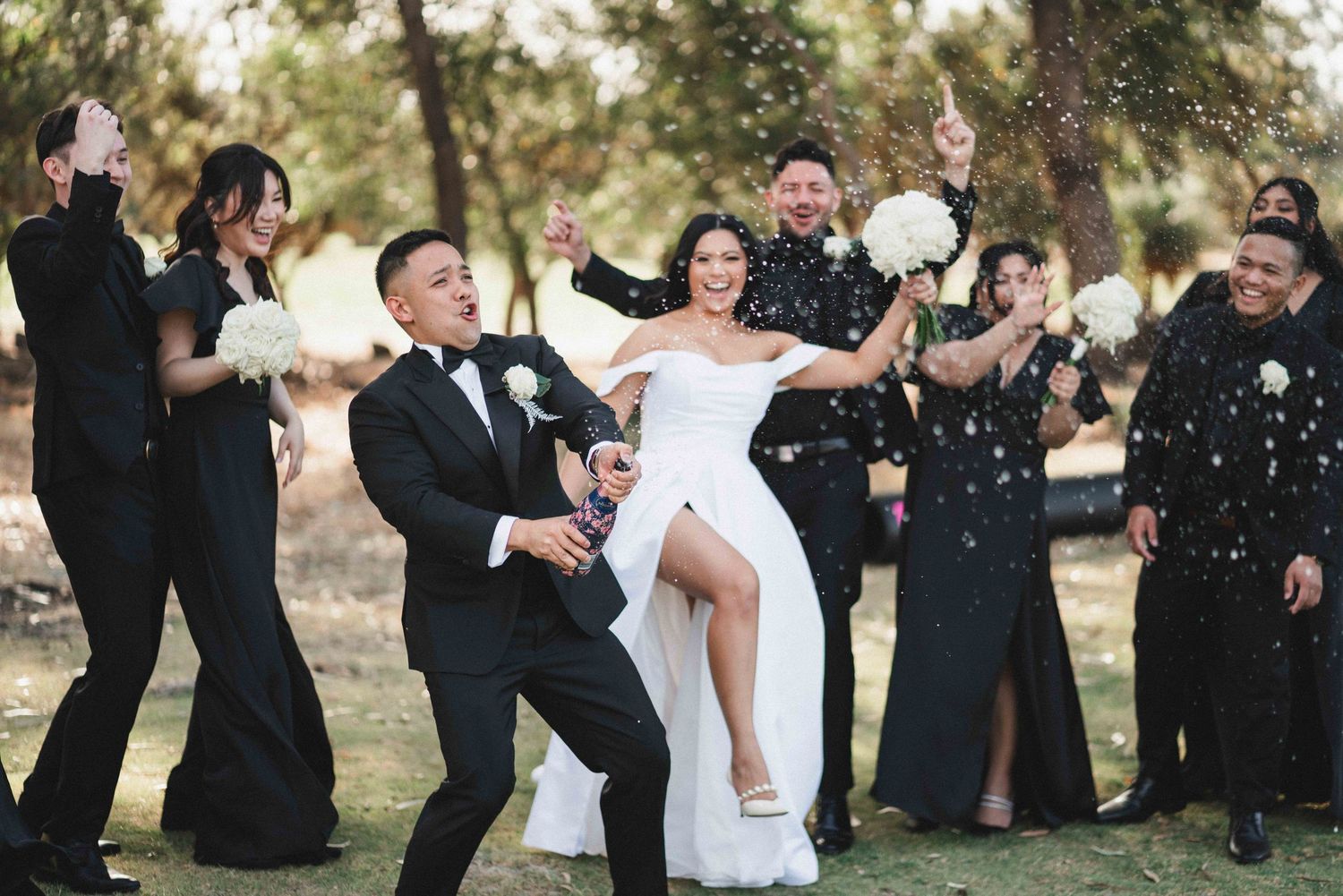 A joyful black and white wedding scene shows newlyweds and guests celebrating with confetti outdoors.