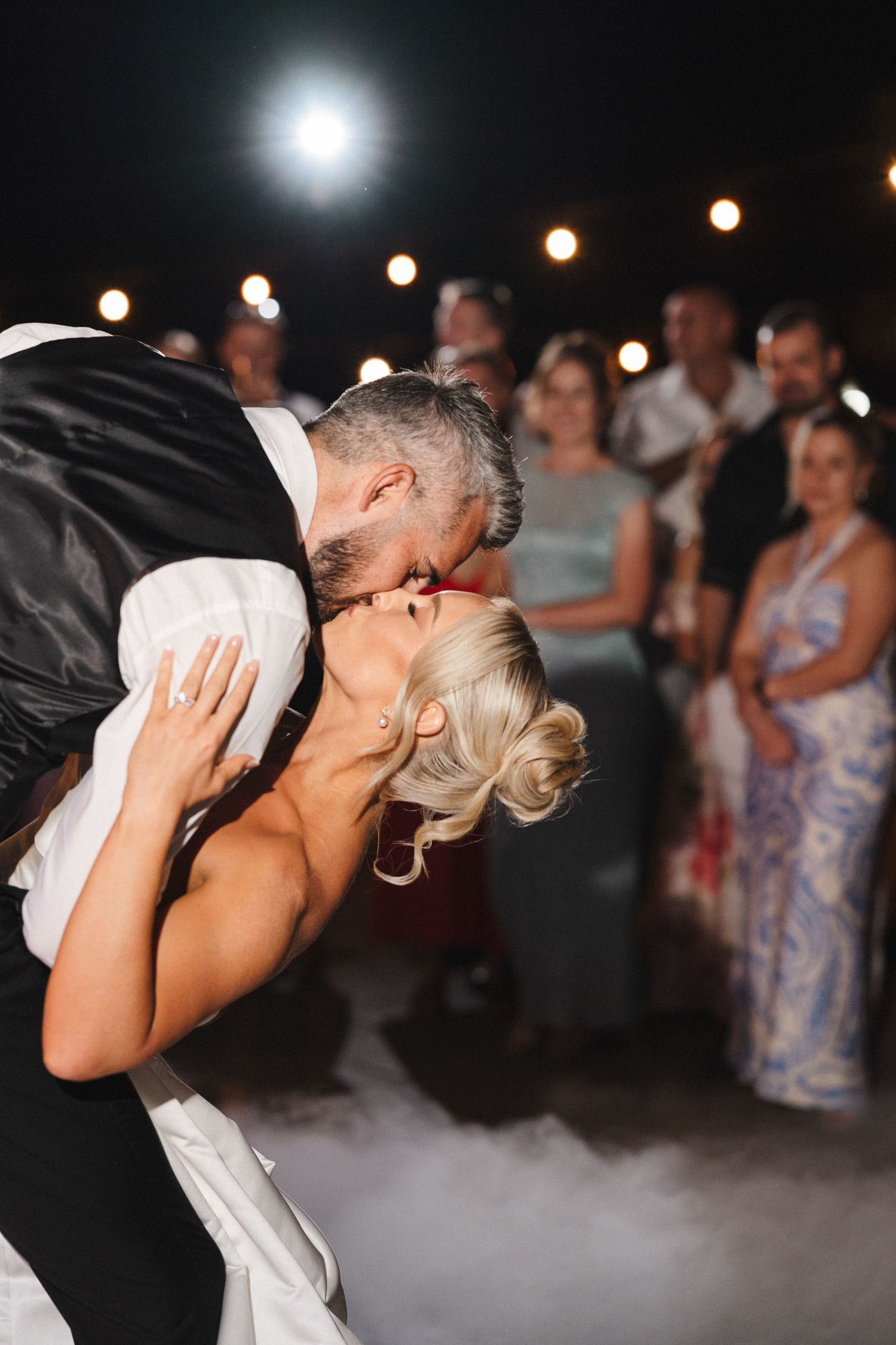 A romantic dip kiss between newlyweds on the dance floor surrounded by twinkling lights at an evening wedding reception.