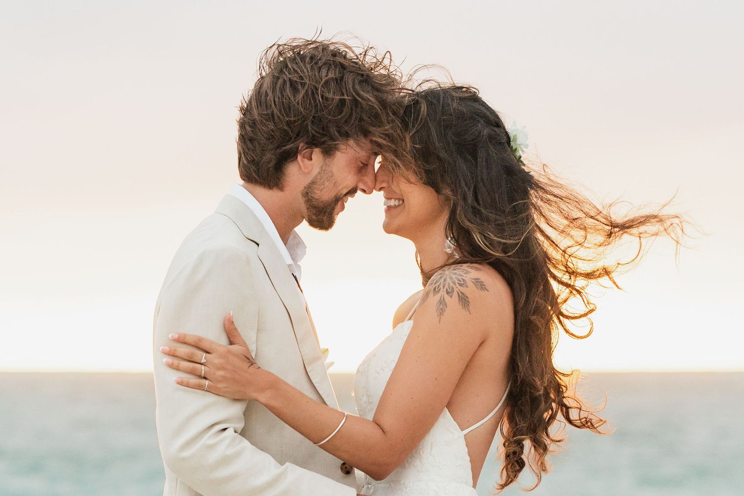Romantic beach wedding photo shoot with couple in white attire against ocean backdrop.