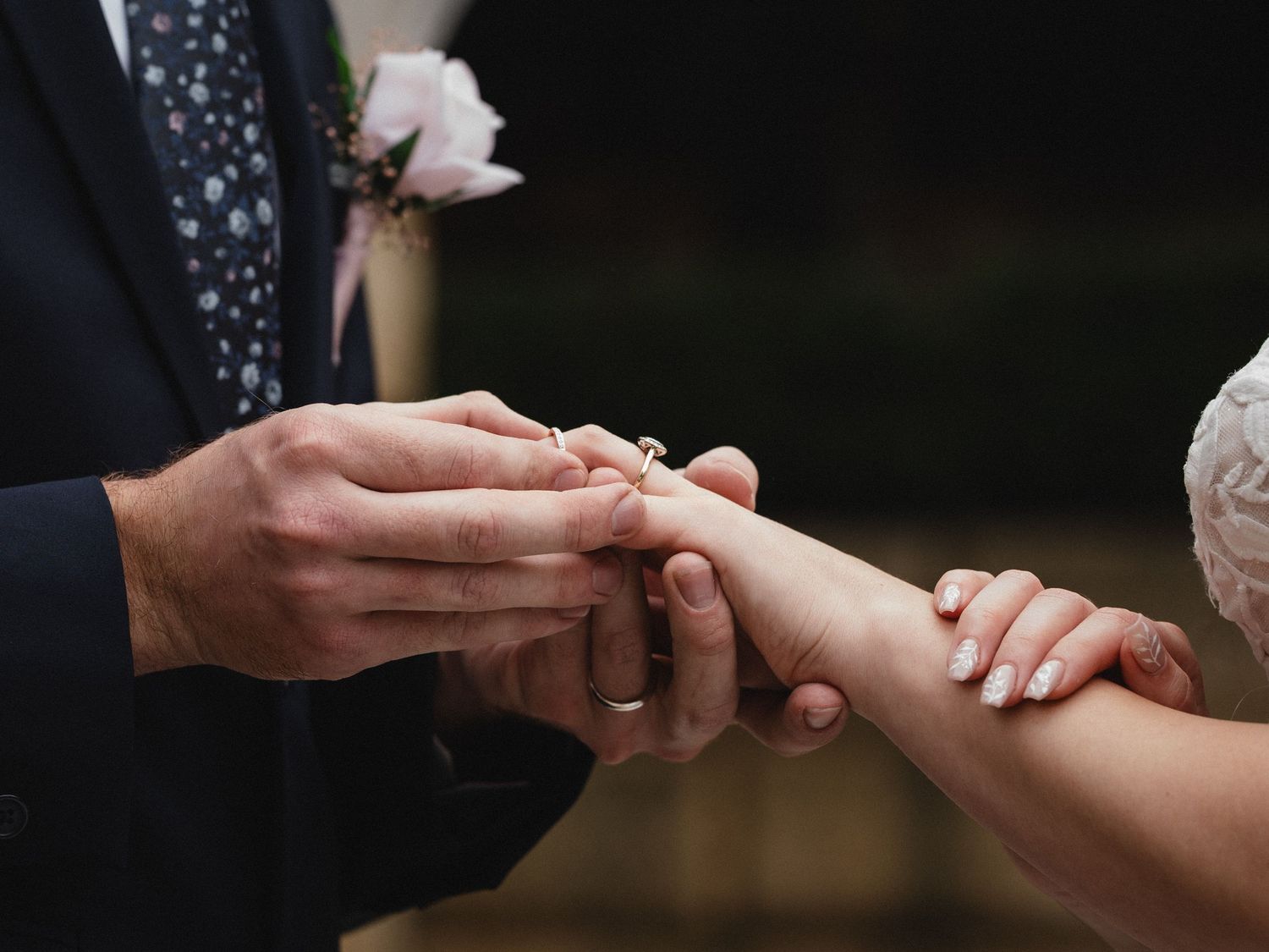Groom placing a diamond engagement ring on bride's finger during a wedding ceremony.