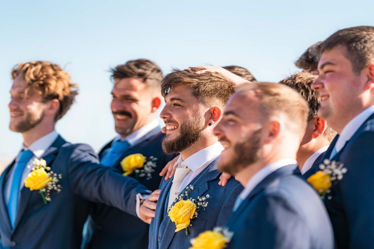 Groomsmen in navy suits with yellow sunflower boutonnieres standing together outdoors.