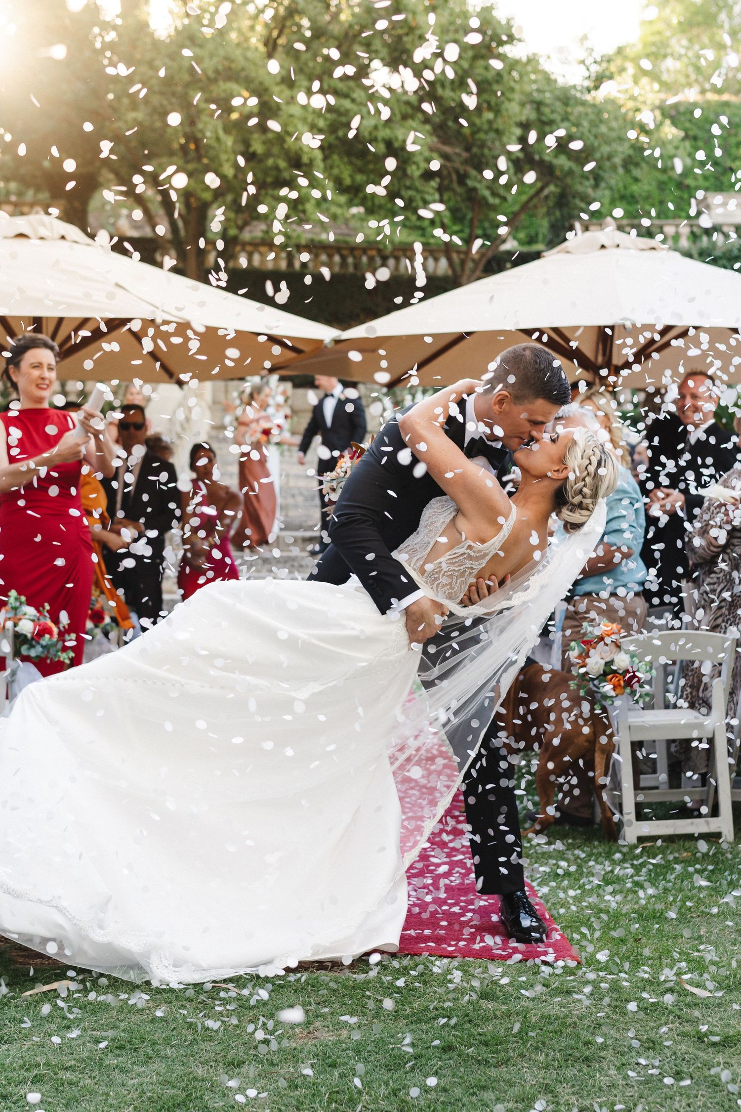 A sequence of wedding photos showing a couple twirling and dancing in a garden as white flower petals float through the air.