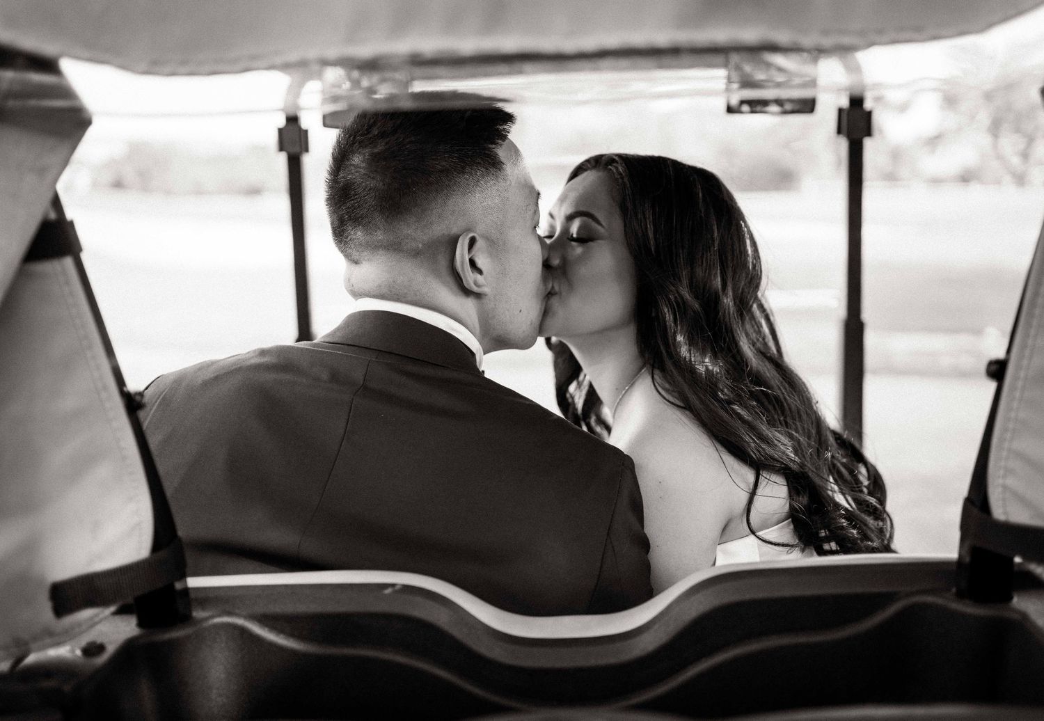 Intimate black and white moment of newlyweds sharing a kiss in a vintage cart.