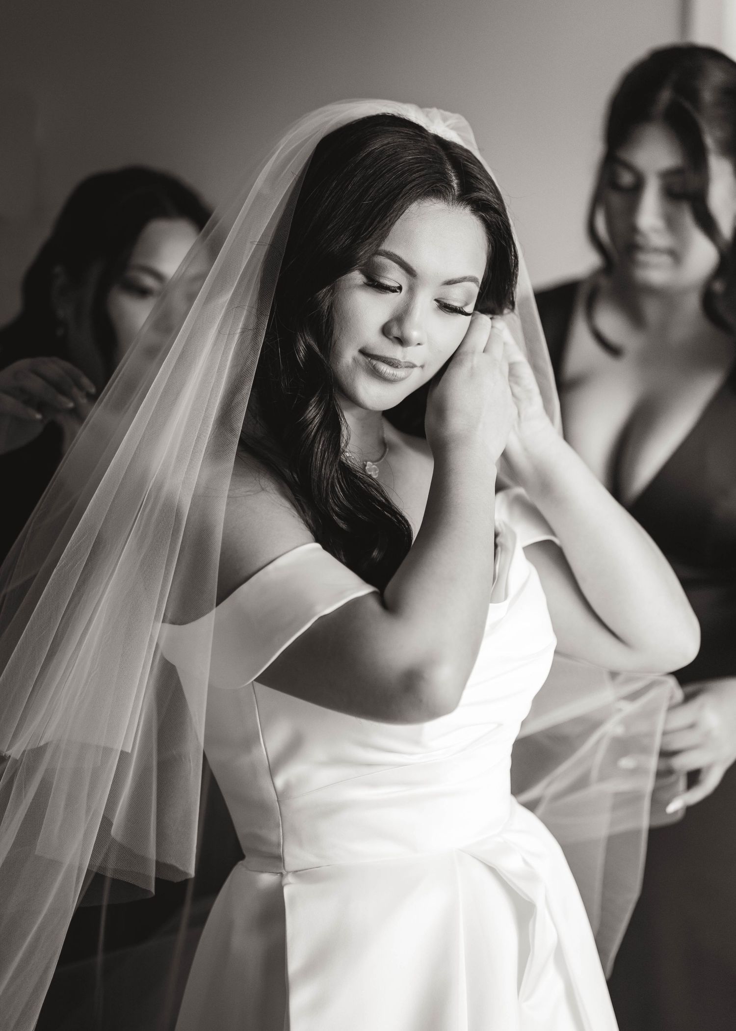 Elegant bride in white dress and veil preparing for ceremony in black and white.