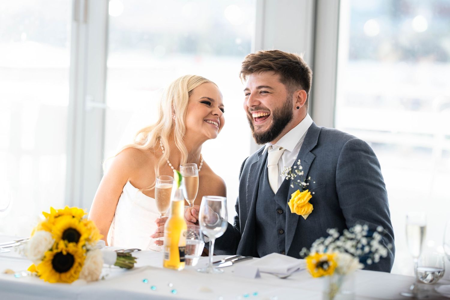 Candid reception moment with couple laughing at wedding table decorated with sunflowers.