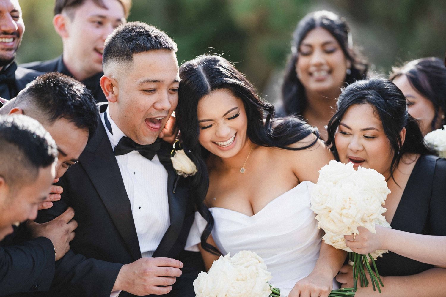 A joyful wedding party celebrates outdoors with laughter and smiles during a sunny celebration.