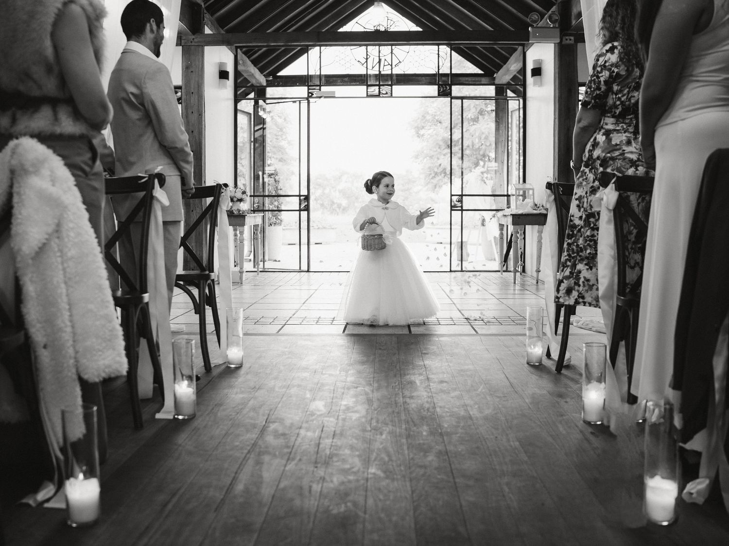 Black and white photo of a flower girl walking down the aisle at a wedding ceremony with candles lining the path.