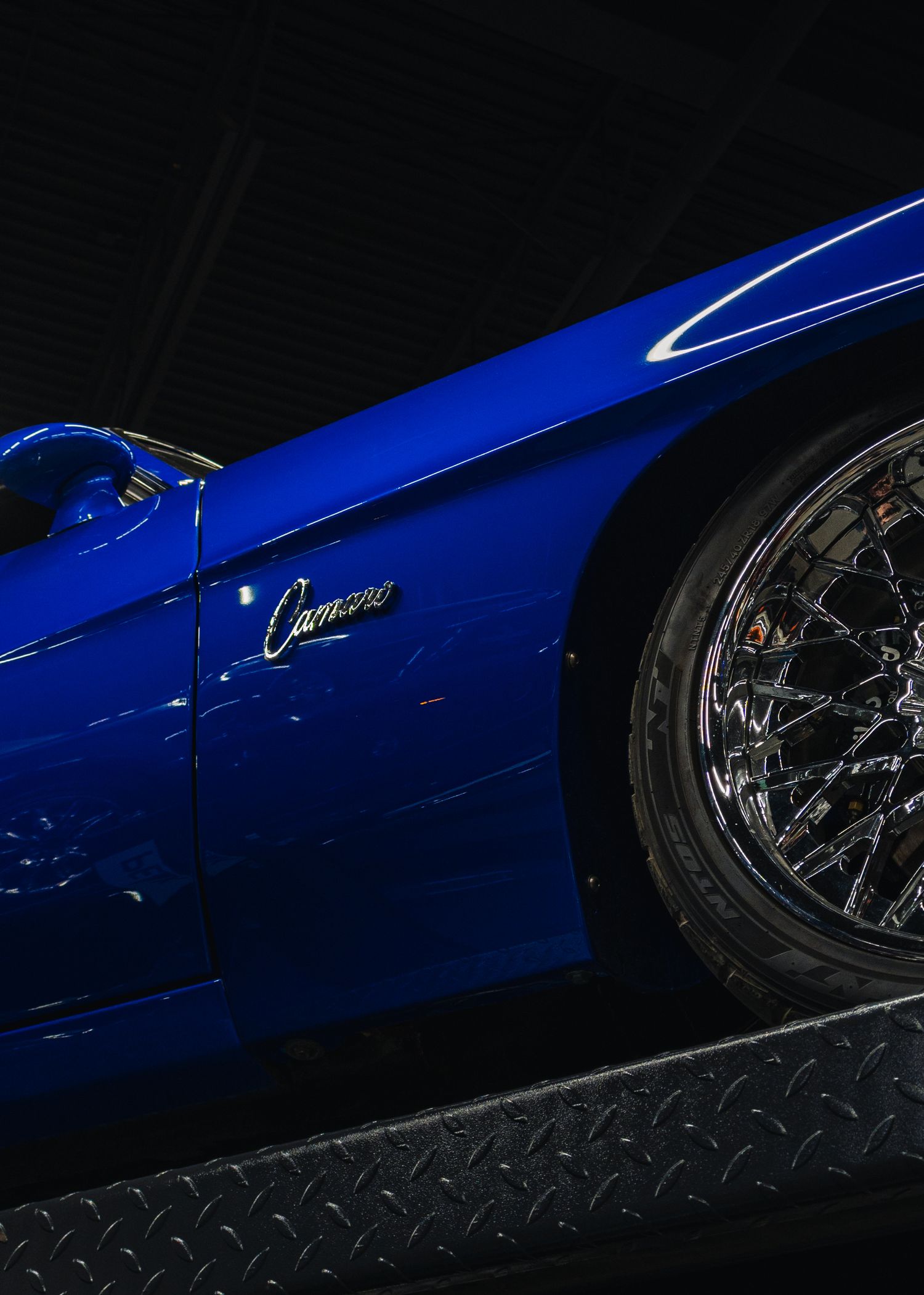 A sleek blue Chevrolet Camaro with chrome mesh wheels, showcasing its glossy finish in a dark studio setting.