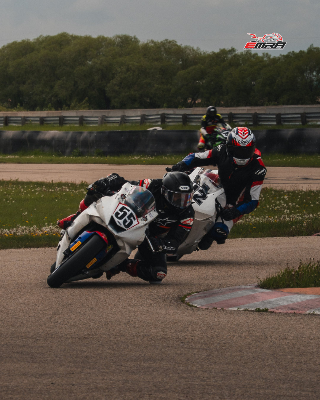Motorcycle racers lean into a turn on a racing circuit during an EMRA track day event.
