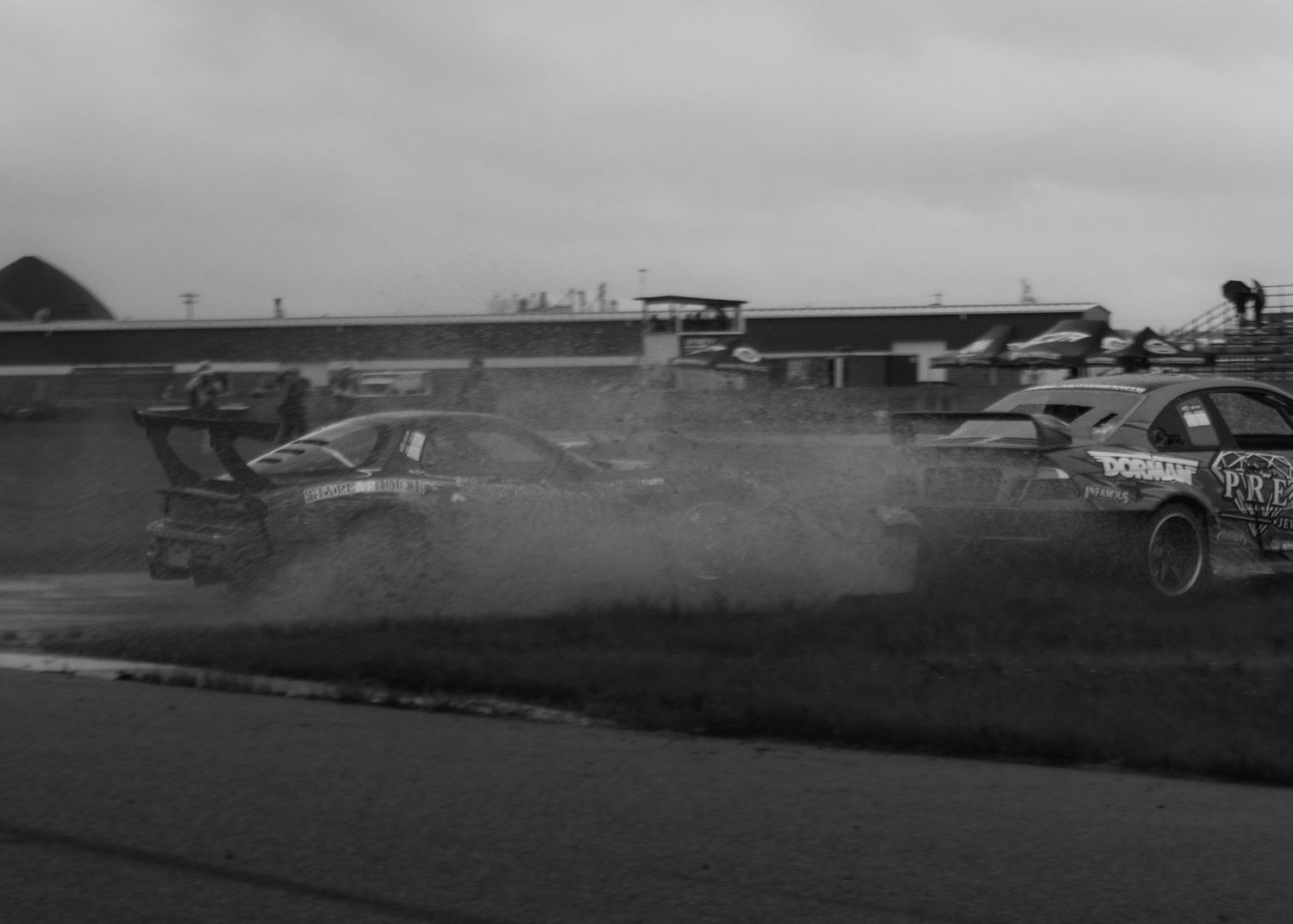 Black and white photo of race cars spinning out on a wet track during a motorsport event.