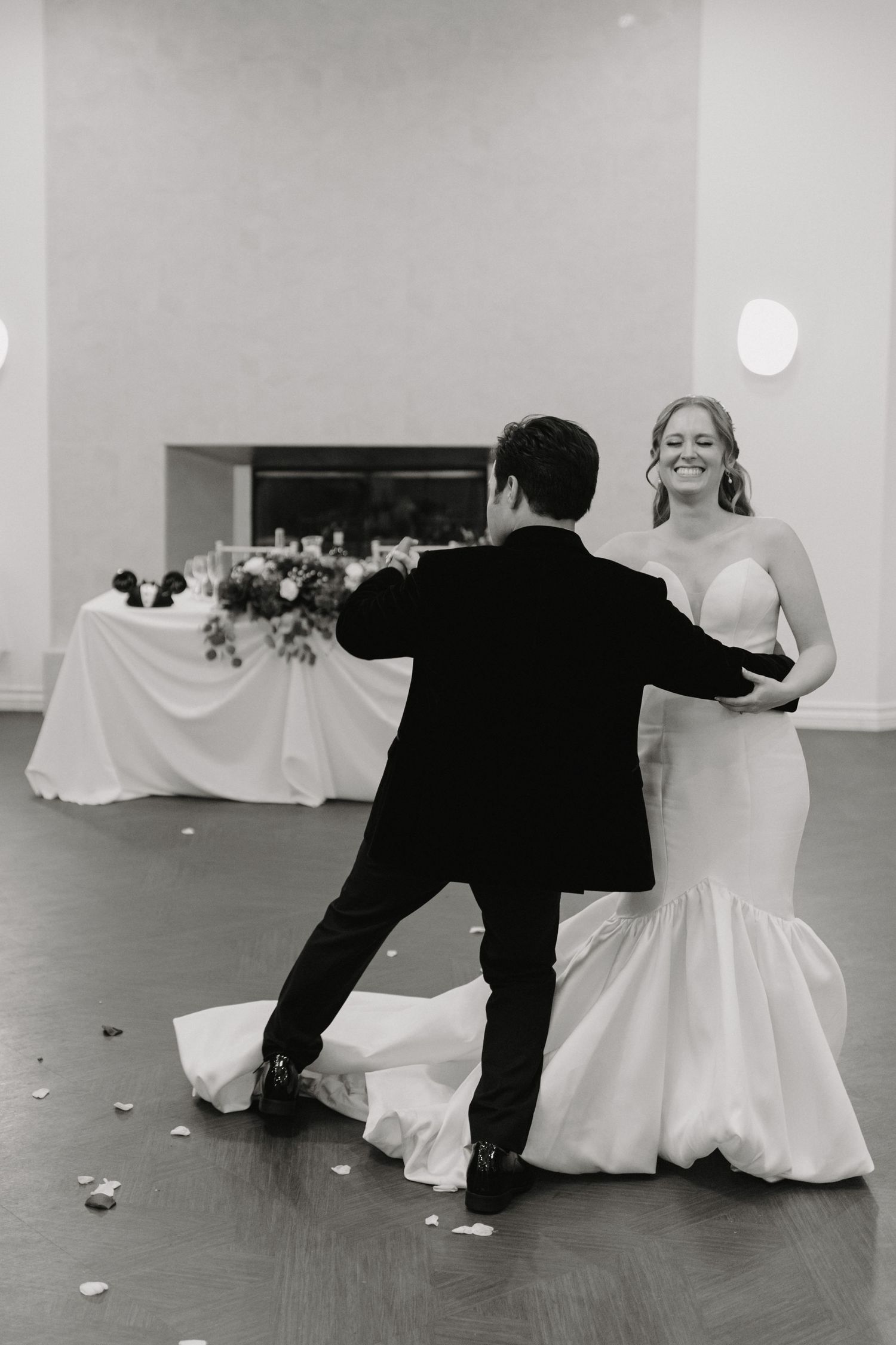 A couple shares a playful dance moment at their wedding reception, with the bride's white dress twirling on a wooden floor.
