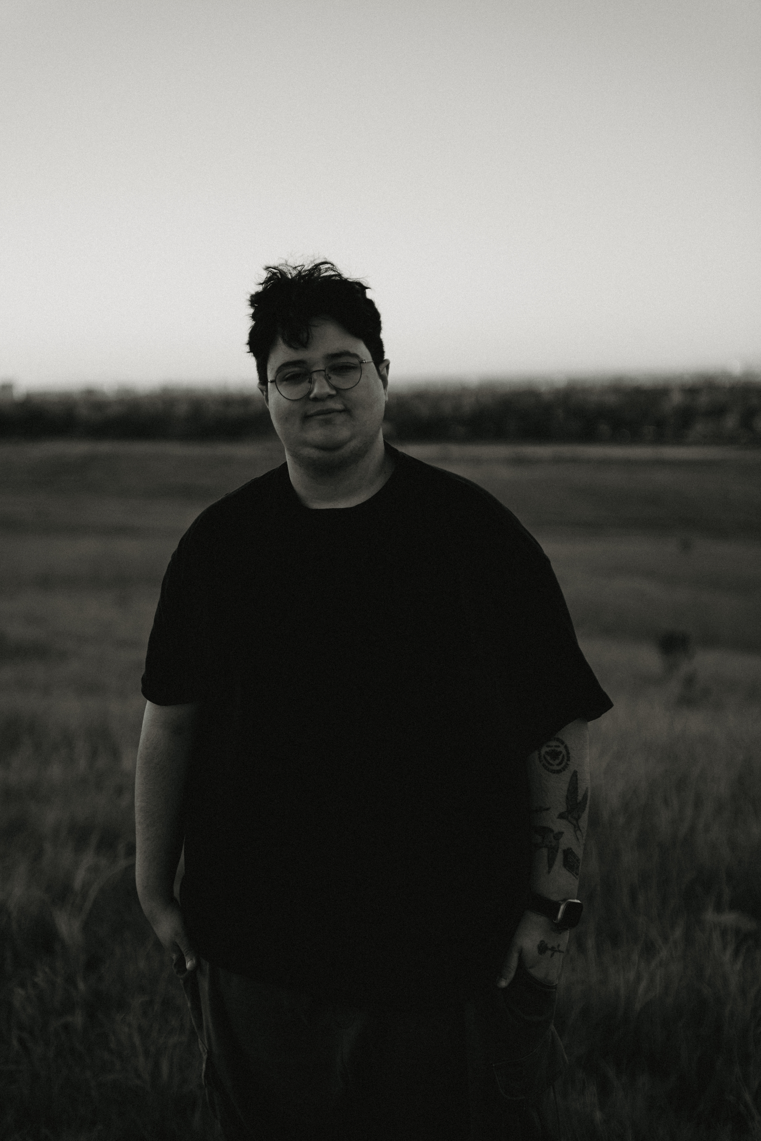 A person wearing dark clothing stands in a field at dusk in a series of moody black and white photos.
