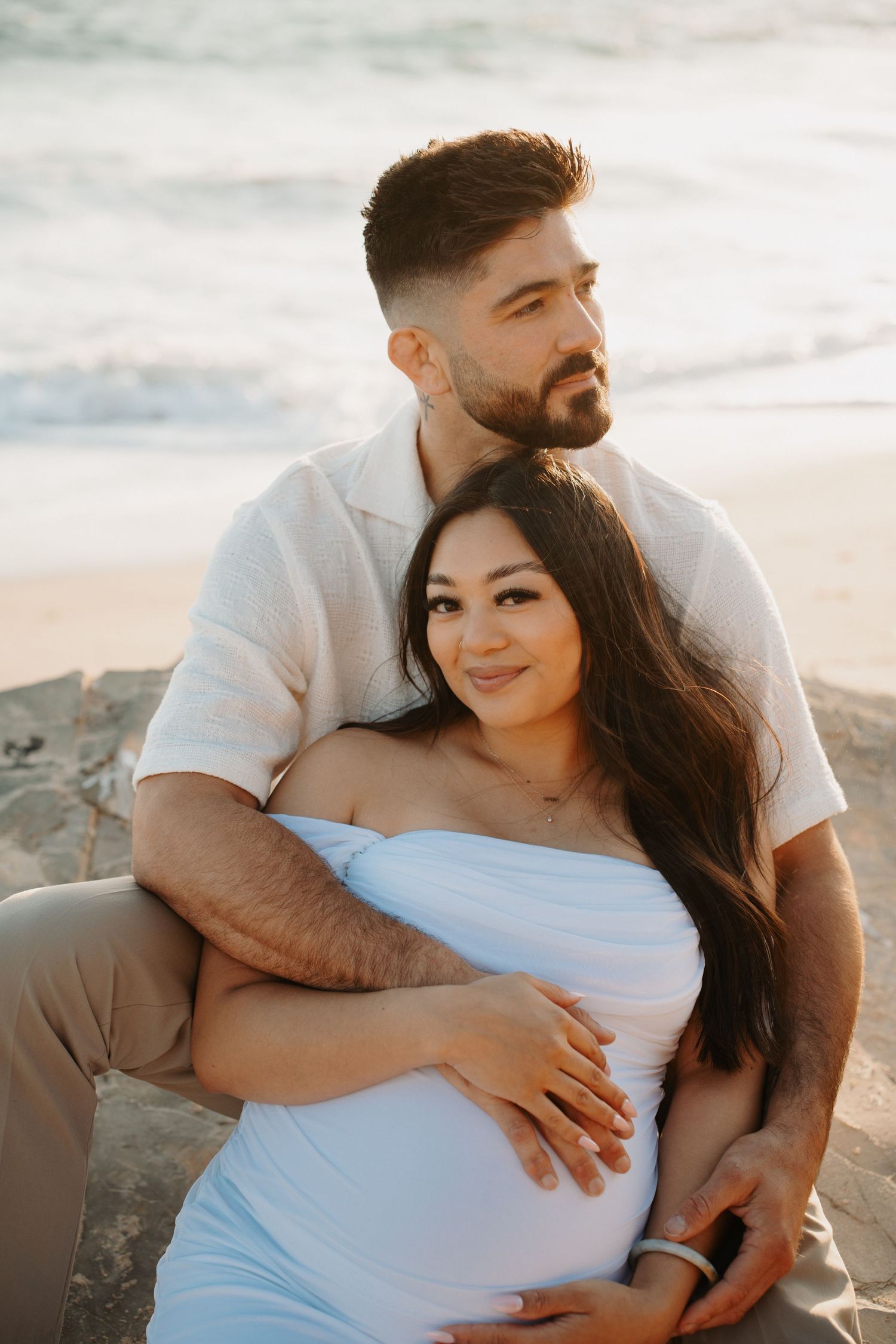 Intimate maternity portraits of couple embracing on beach with ocean backdrop.