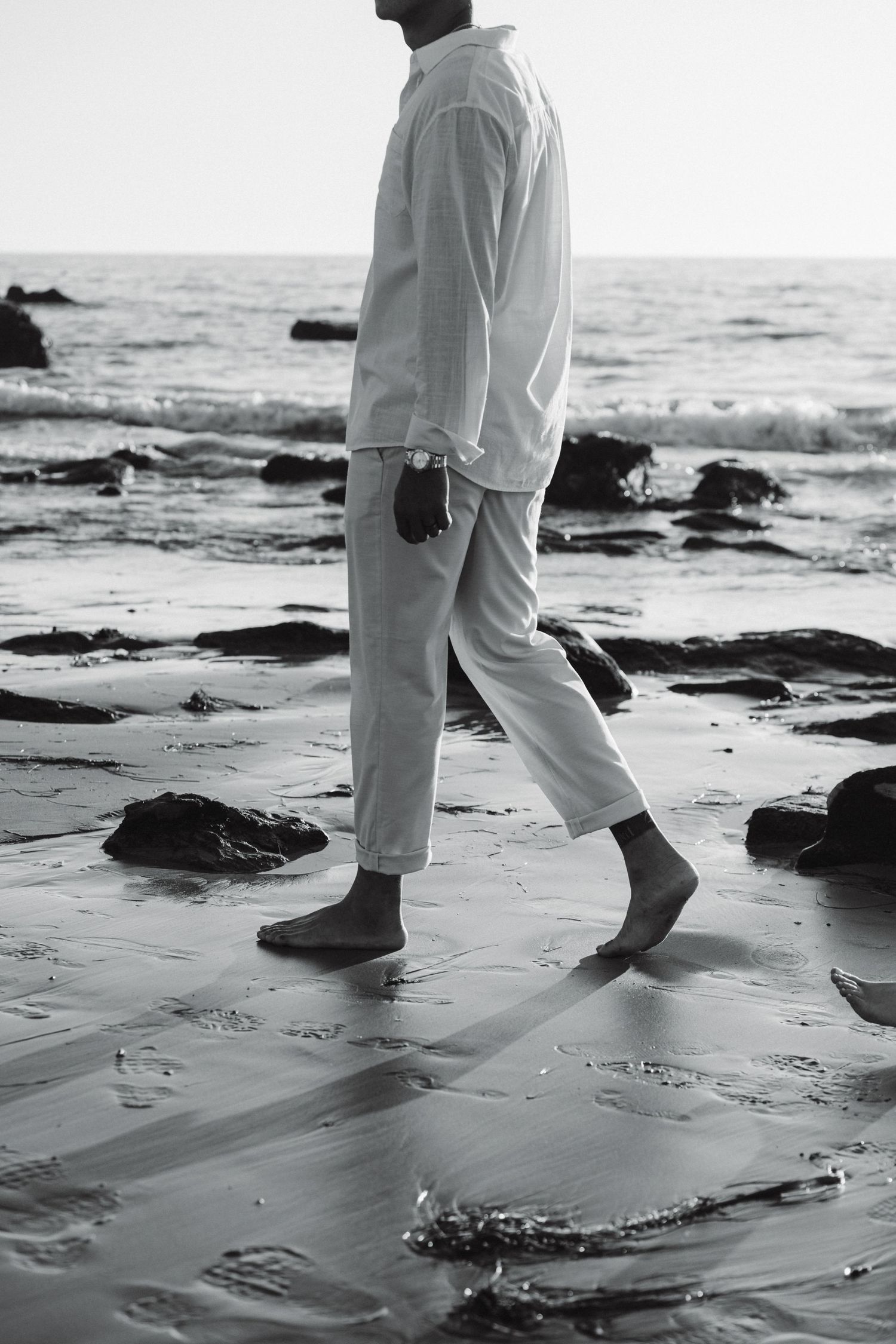 Black and white images of bare feet walking on wet beach sand at sunset.