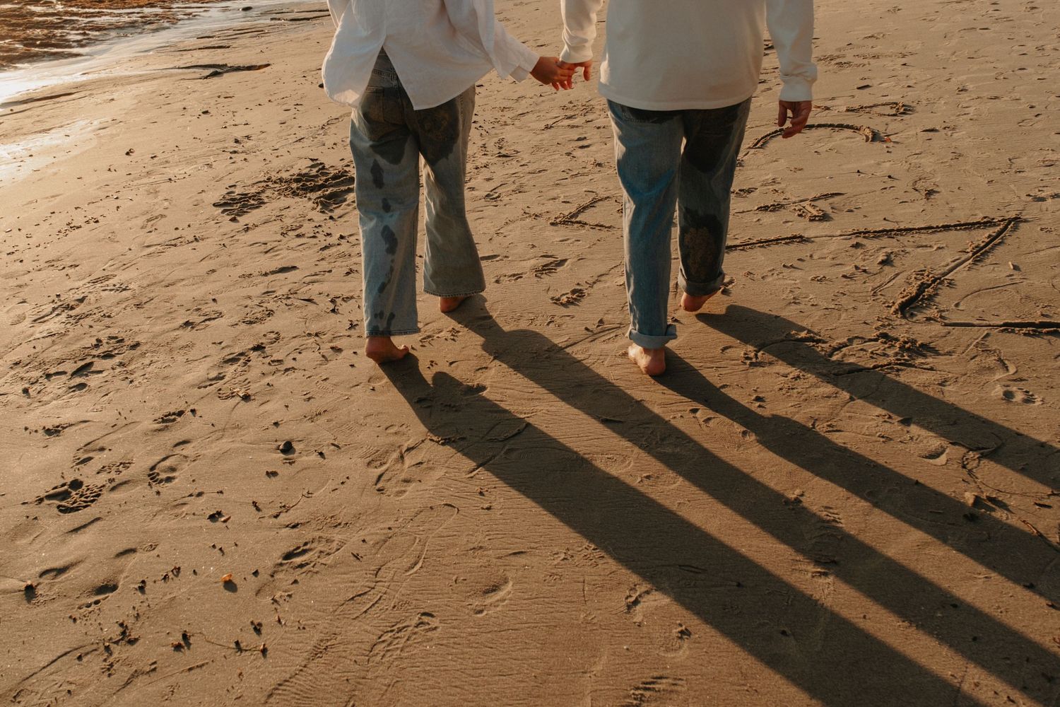 People walking on a sandy beach cast long shadows during sunset creating a peaceful coastal scene.
