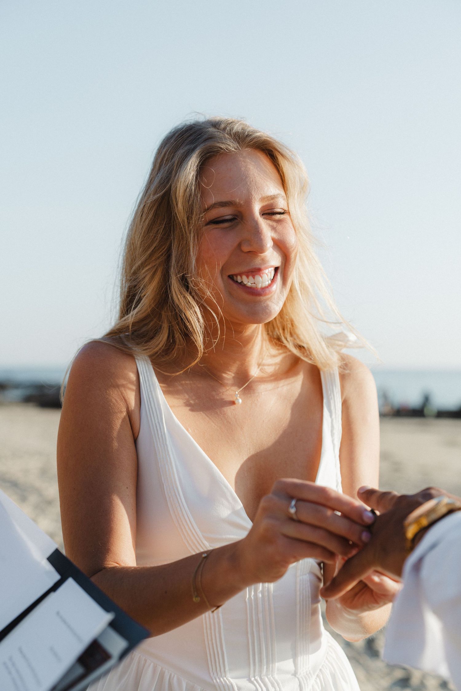 A person in a white dress smiles joyfully while looking down at something in their hands.