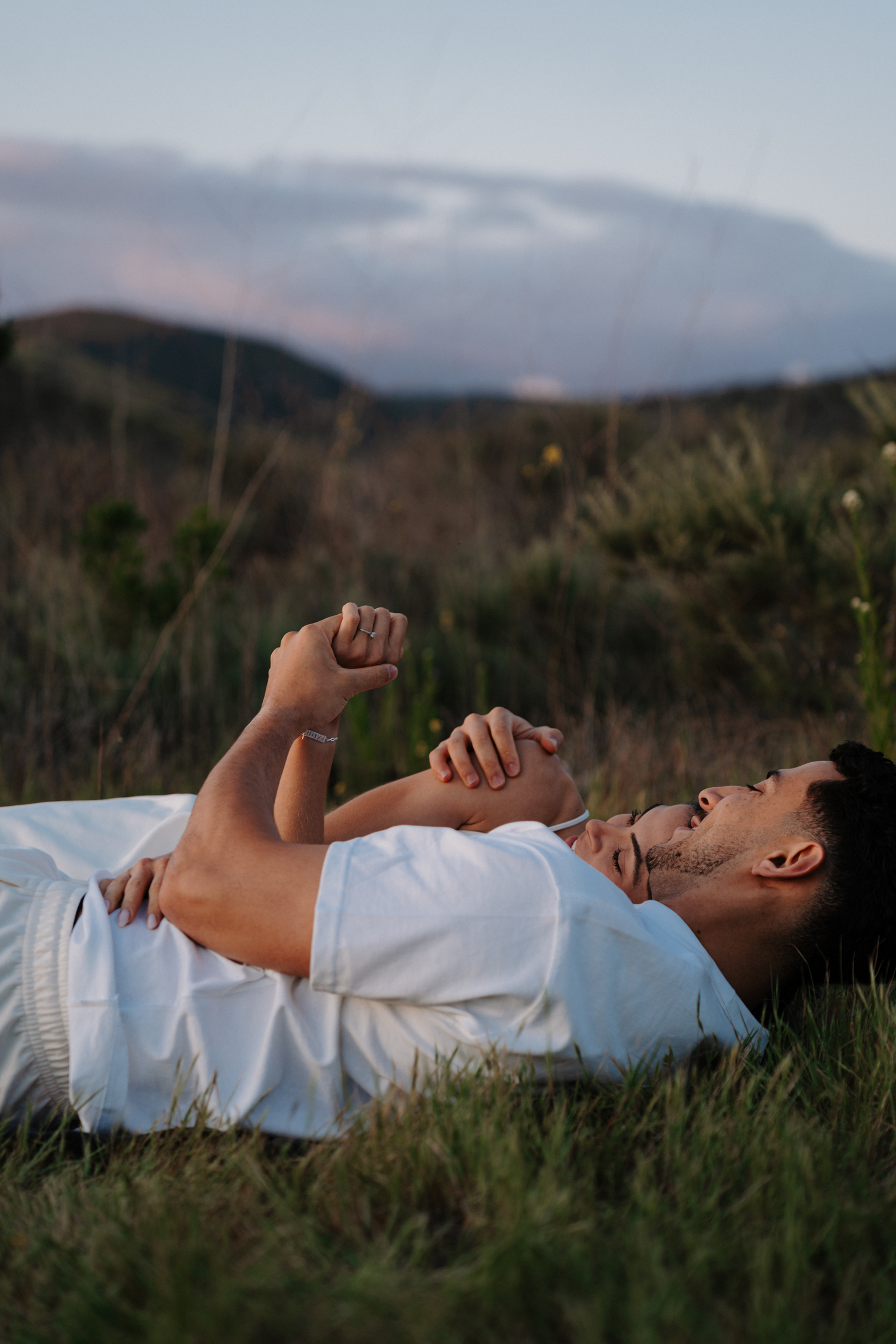 Person lying in tall grass at dusk stretches their arms above their head in a peaceful moment of relaxation.