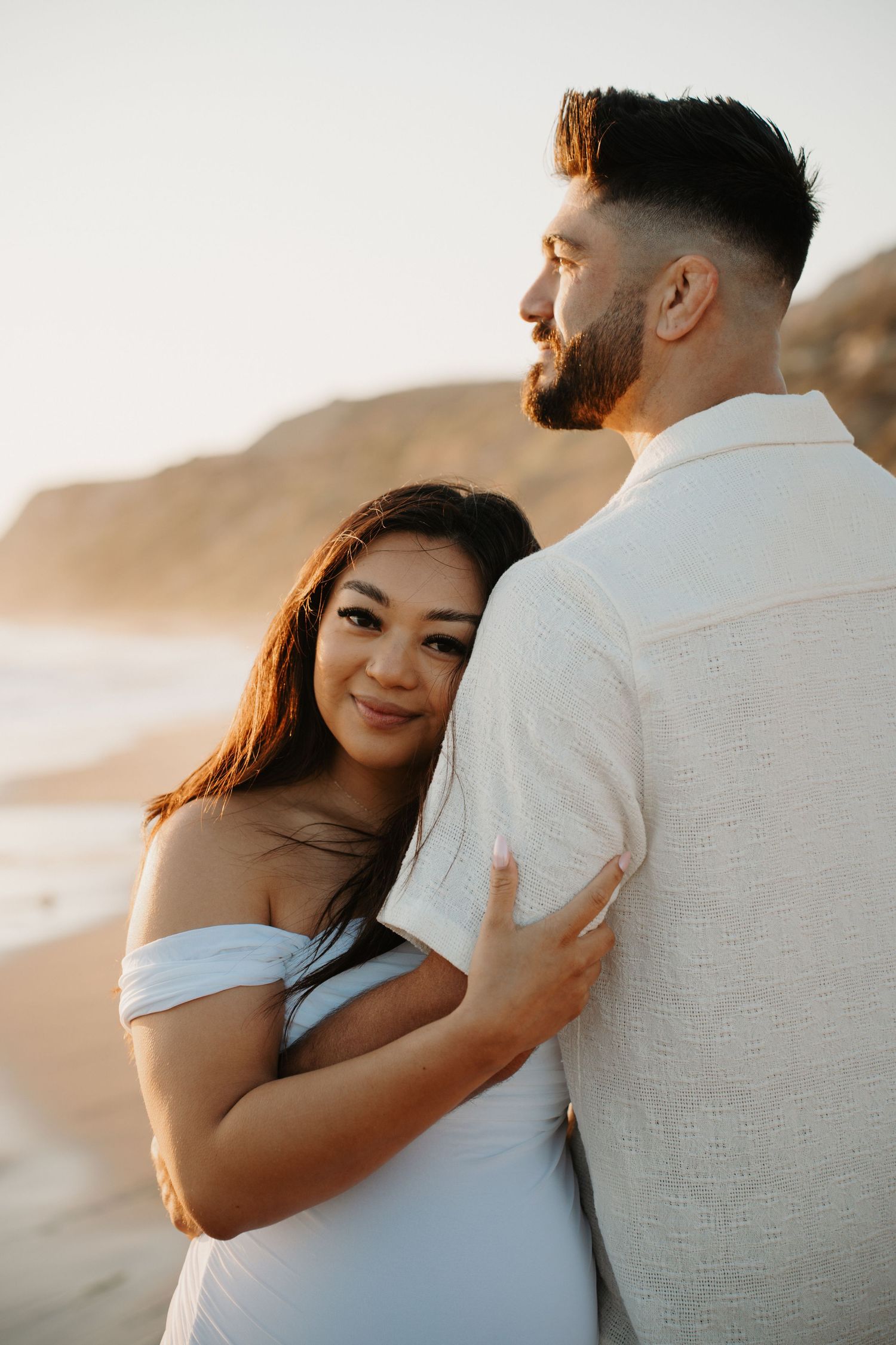 A romantic couple embraces on the beach during golden hour.