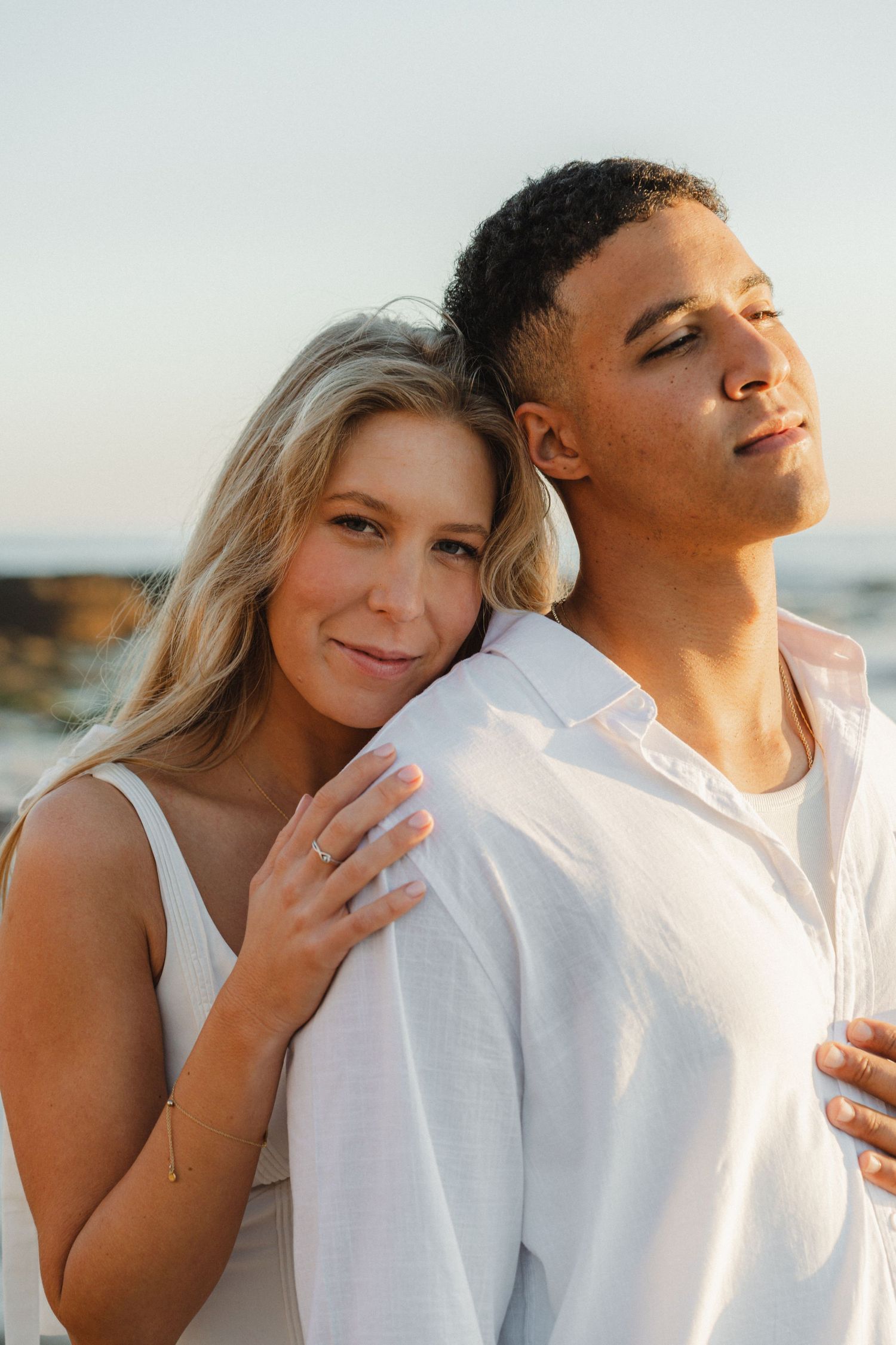 A romantic couple in white clothing embraces on a beach during sunset creating an intimate artistic series of photos.