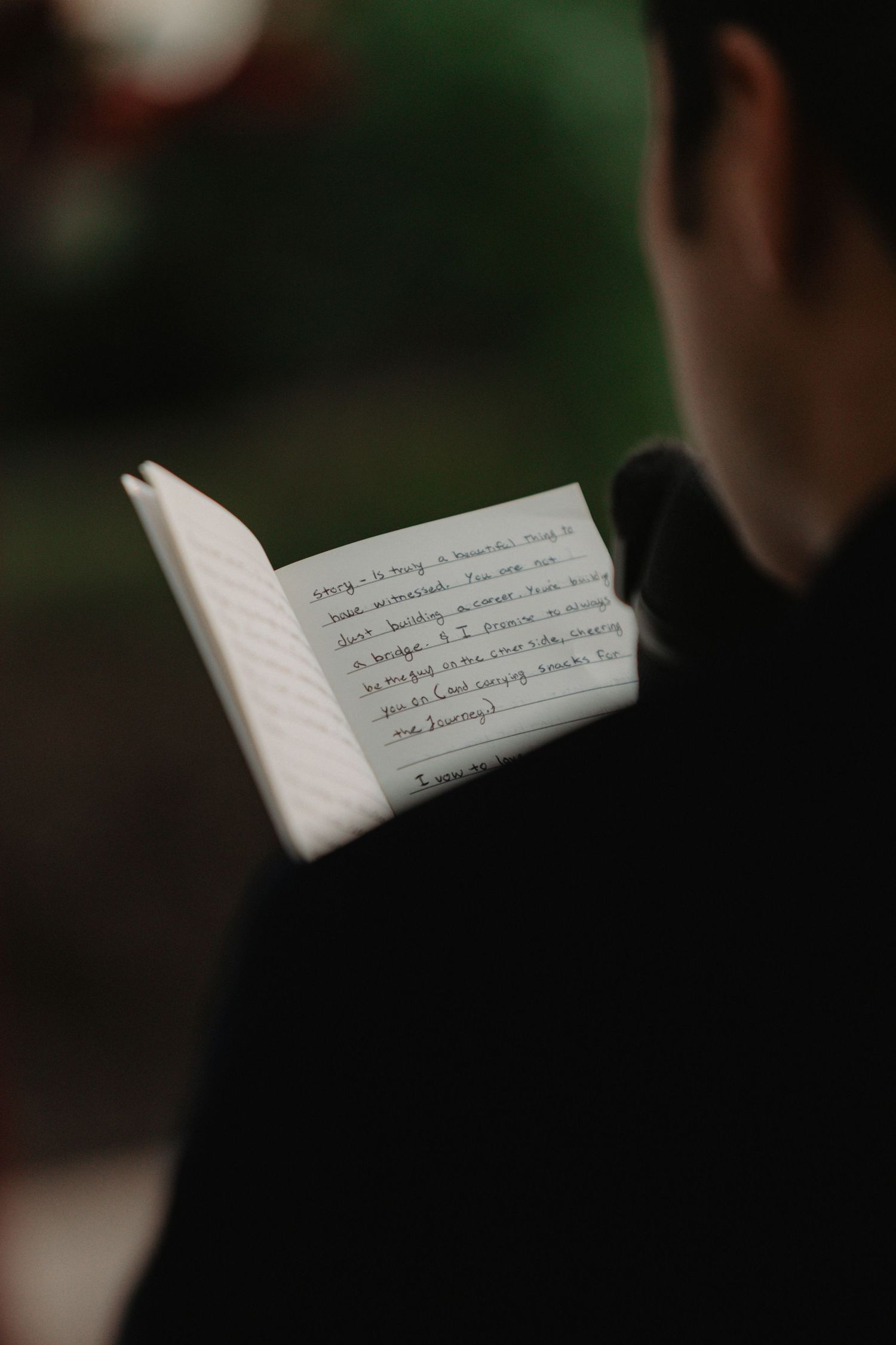A small notebook with handwritten text being held open against a dark blurred background.