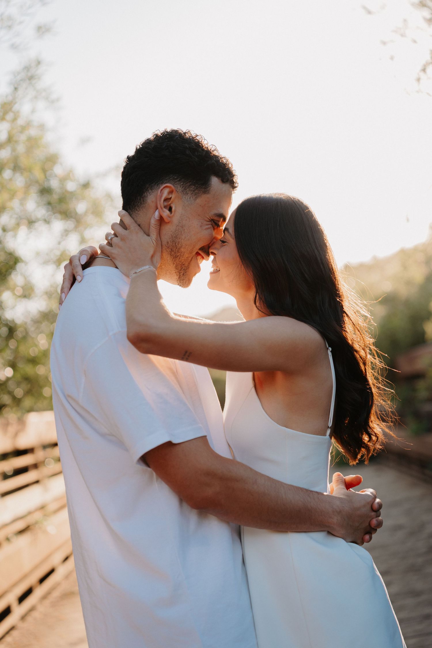 Romantic couple embracing in white outfits during golden hour.