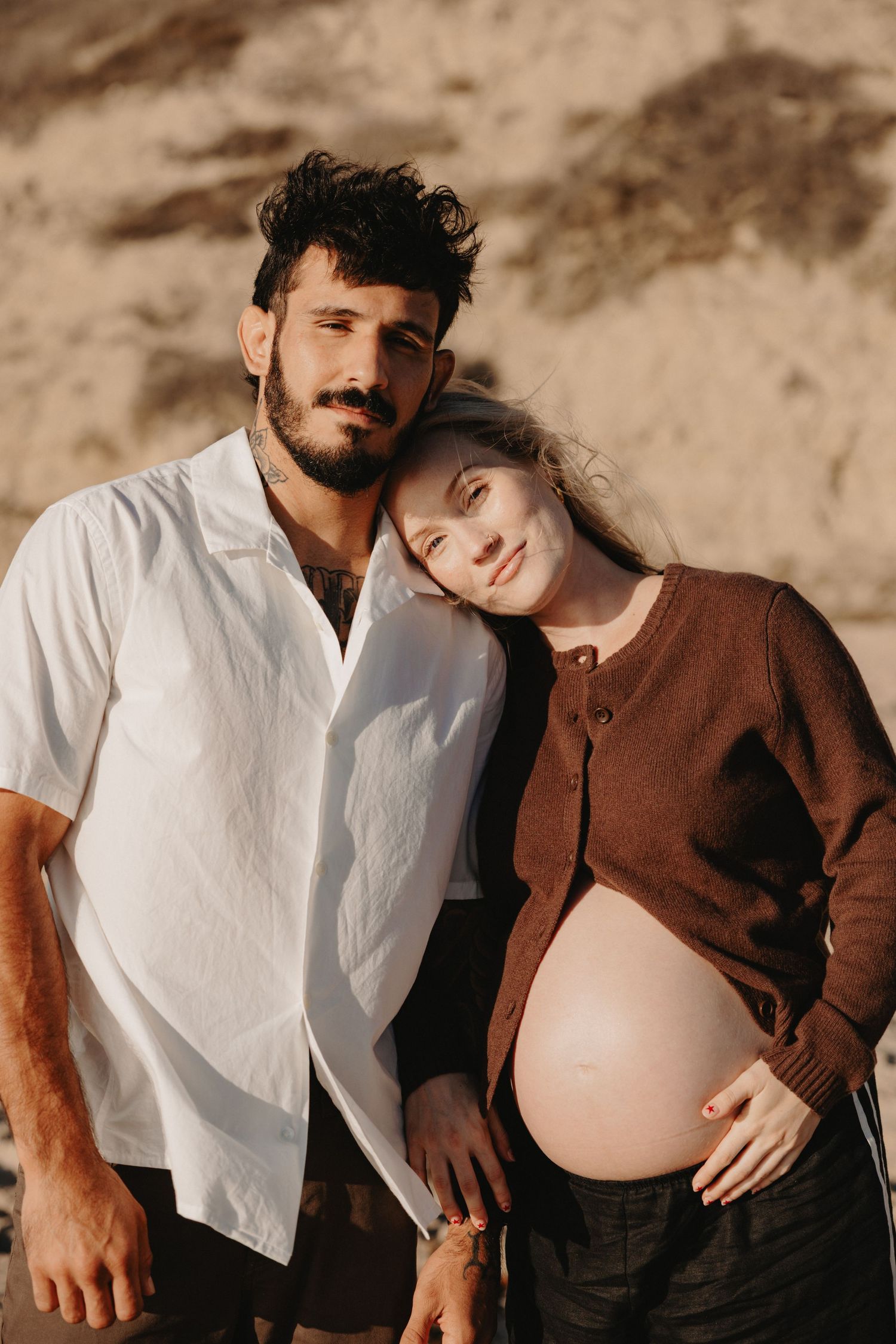 A maternity photo series showing tender moments between a couple in white and brown clothing against an earthy backdrop.