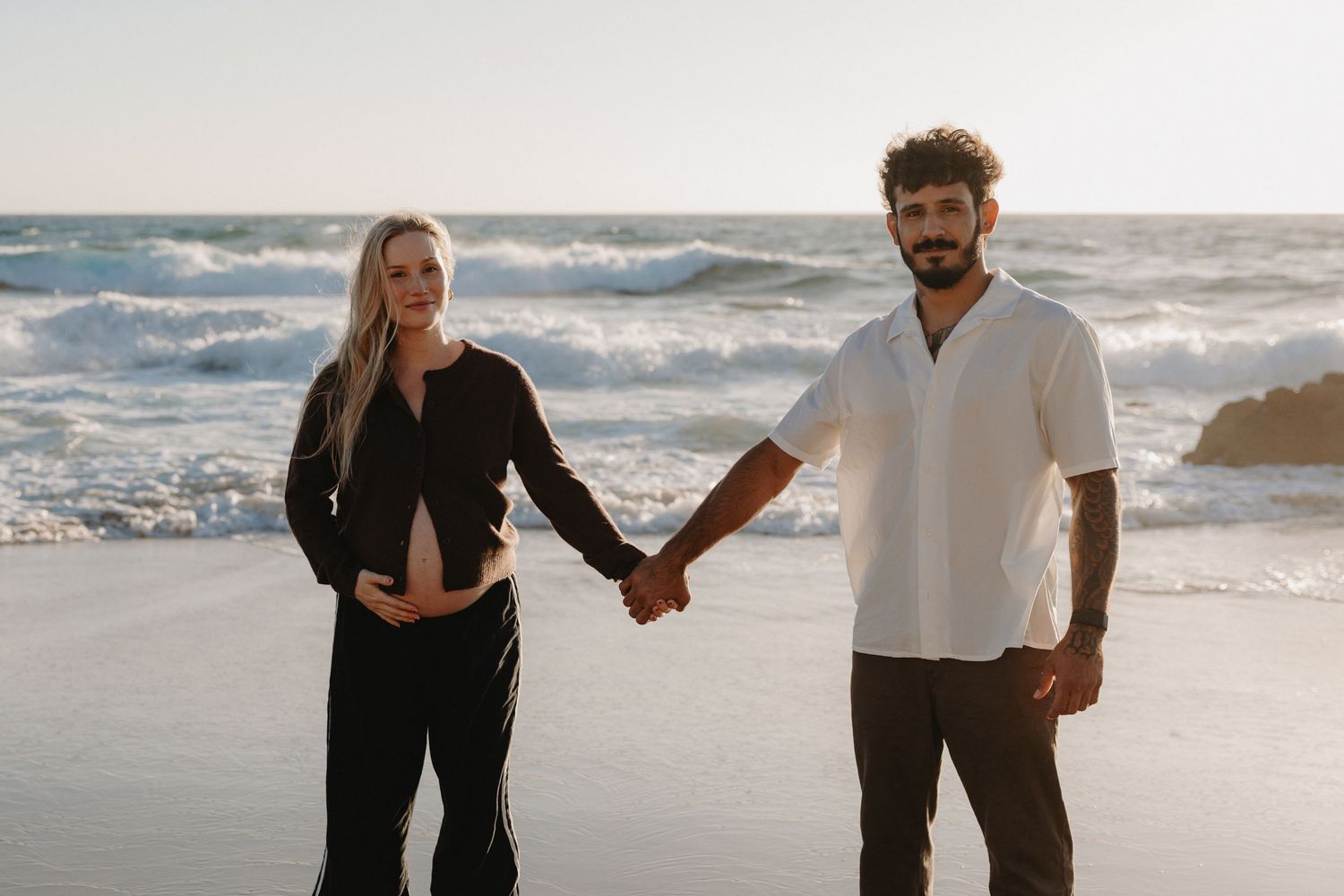 Couple walking together on a sandy beach at sunset holding hands and enjoying romantic ocean views.