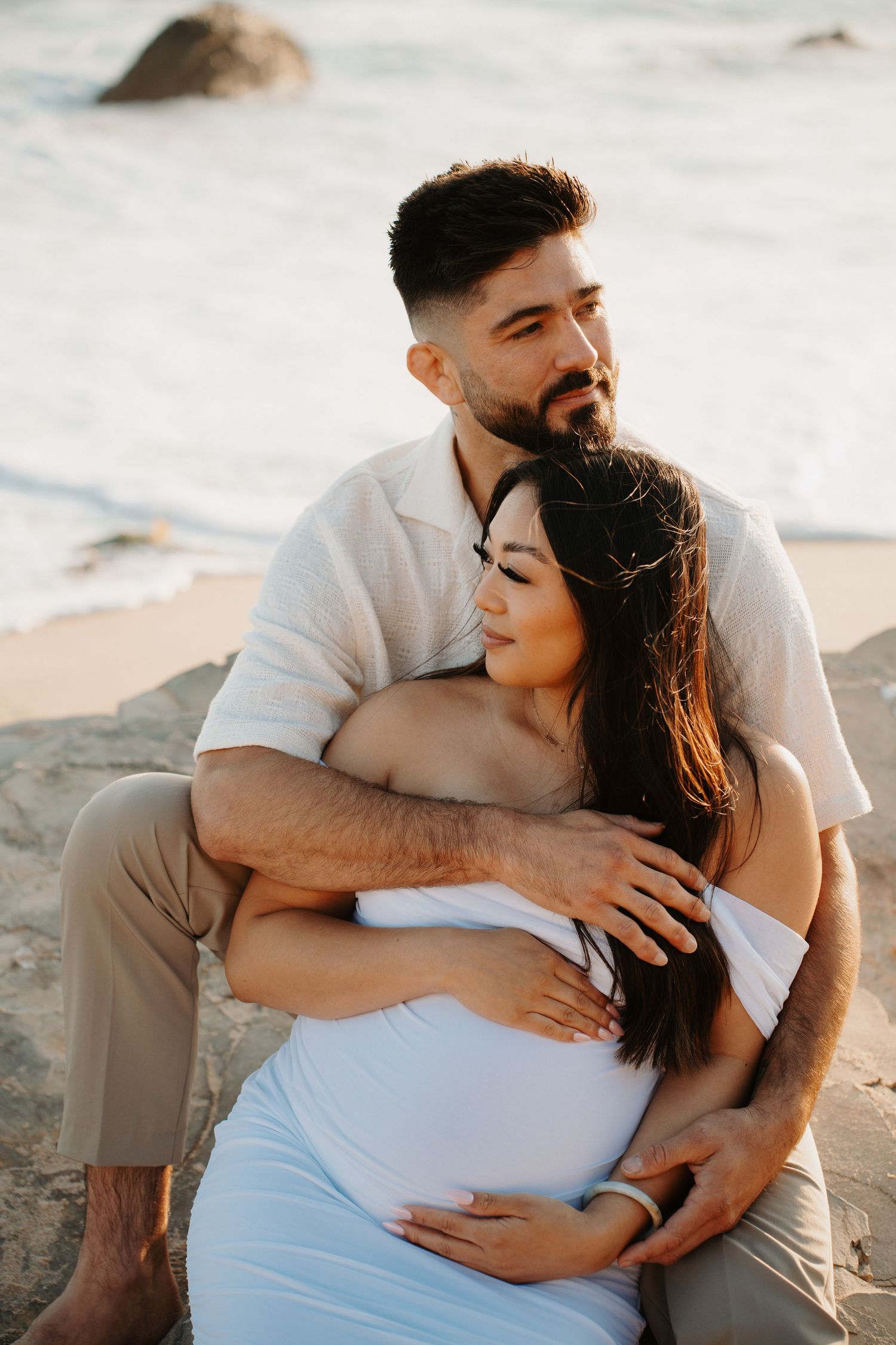 Intimate maternity photo of couple embracing on beach at sunset.