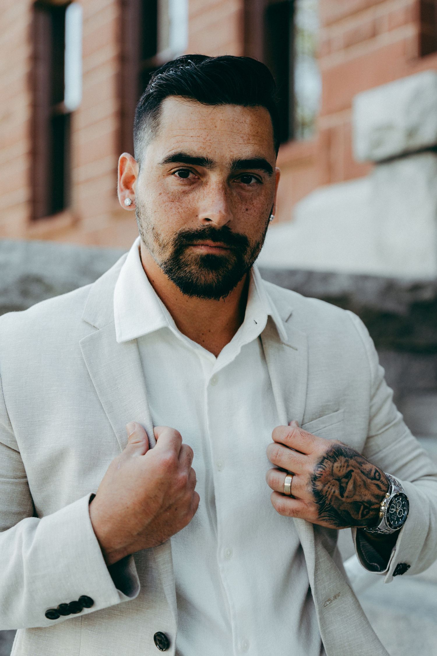 A groom in a white suit adjusts his collar during a wedding photoshoot.