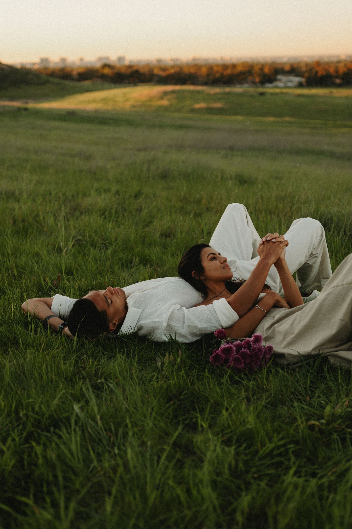 Person in white dress lies peacefully in lush green grass field during golden hour sunset.