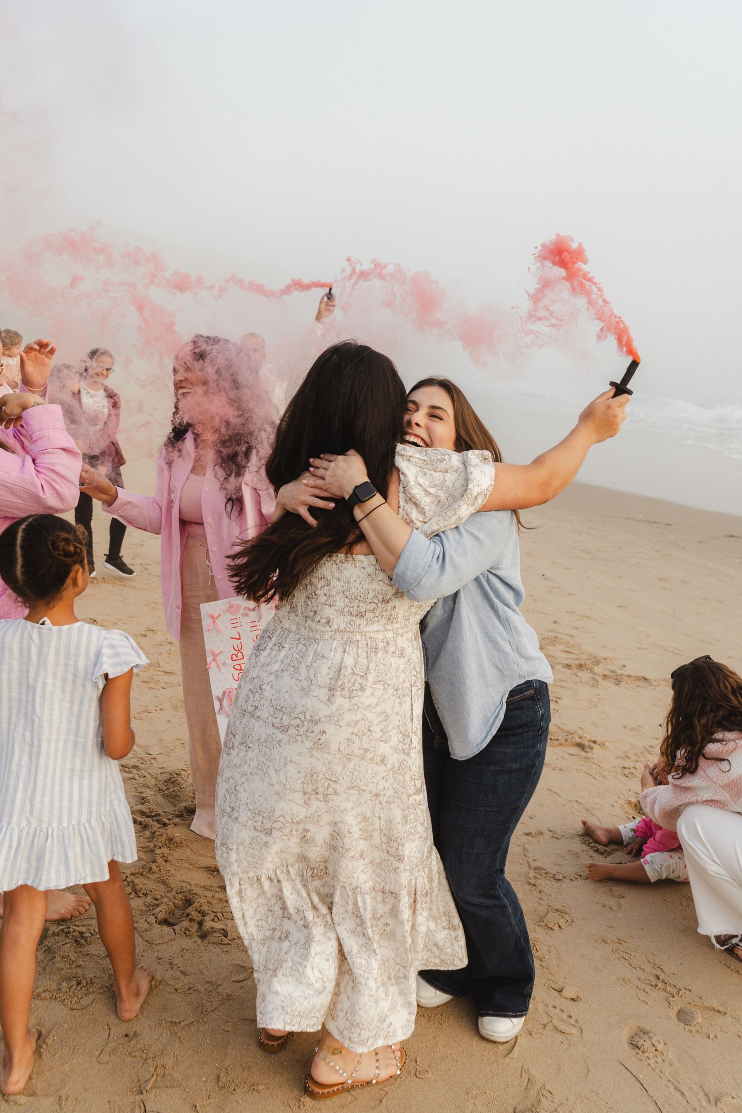 A group of people on a beach celebrating with colorful smoke bombs creating a joyful atmosphere.