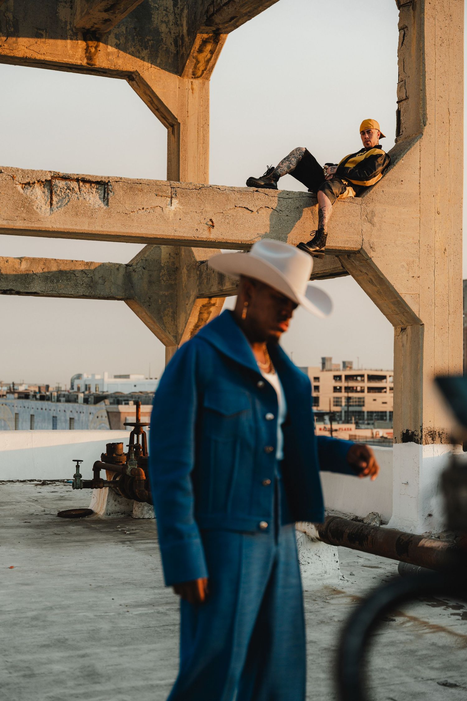 Urban fashion shoot with models in blue denim and cowboy attire on industrial rooftop.