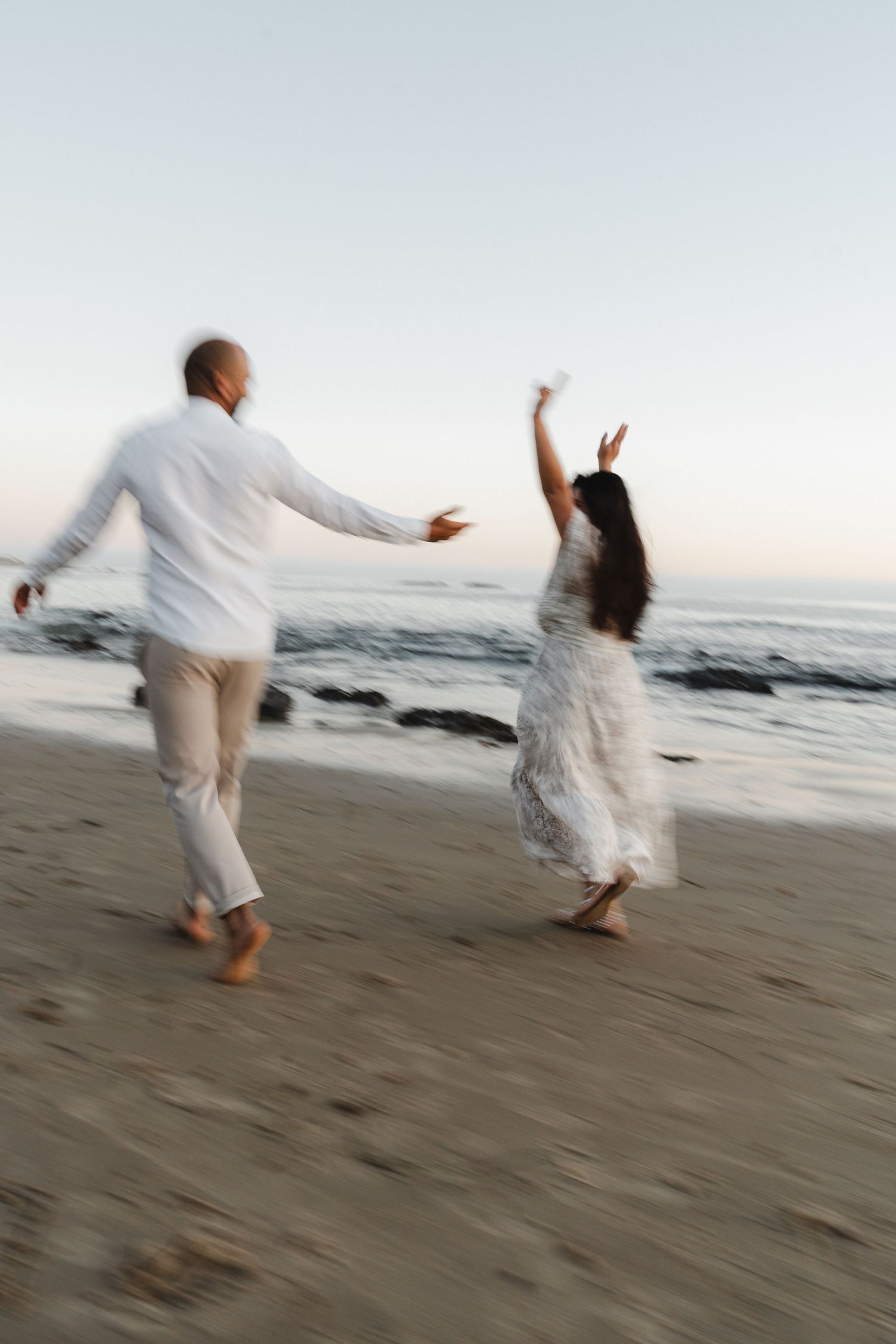 A couple dances joyfully on the beach at sunset with motion blur.