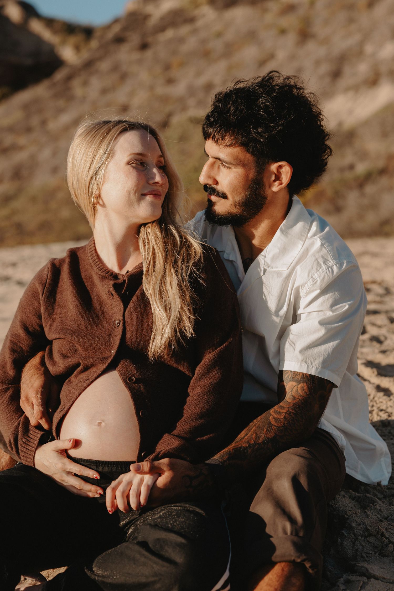 A couple shares intimate moments during a sunset maternity photoshoot against a rocky desert backdrop.