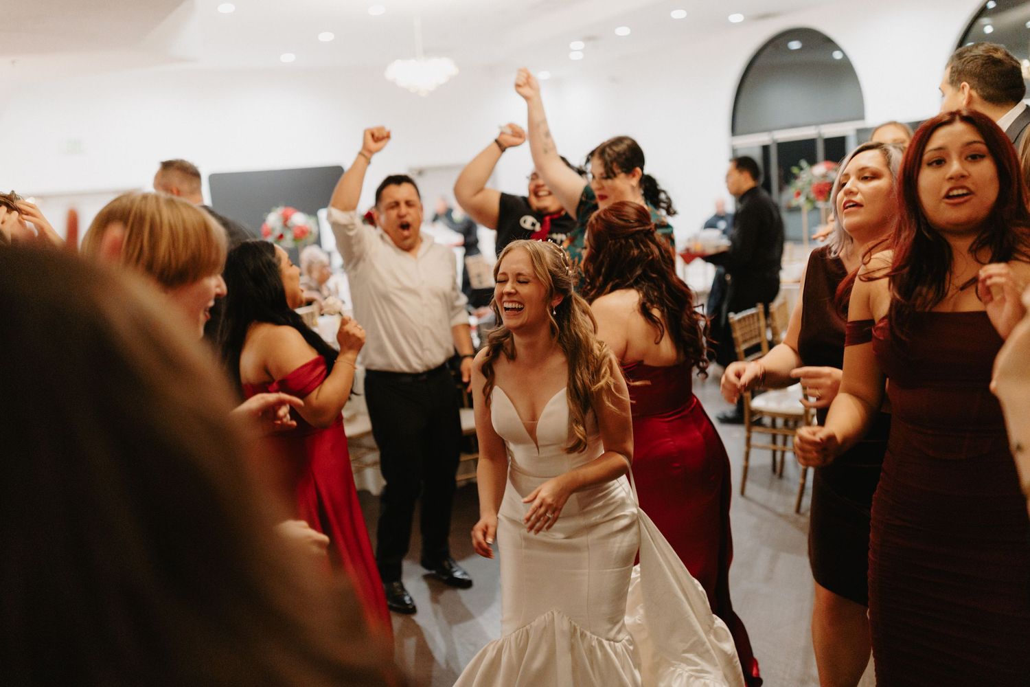 People dancing and celebrating together at a lively wedding reception with joyful expressions and raised arms.