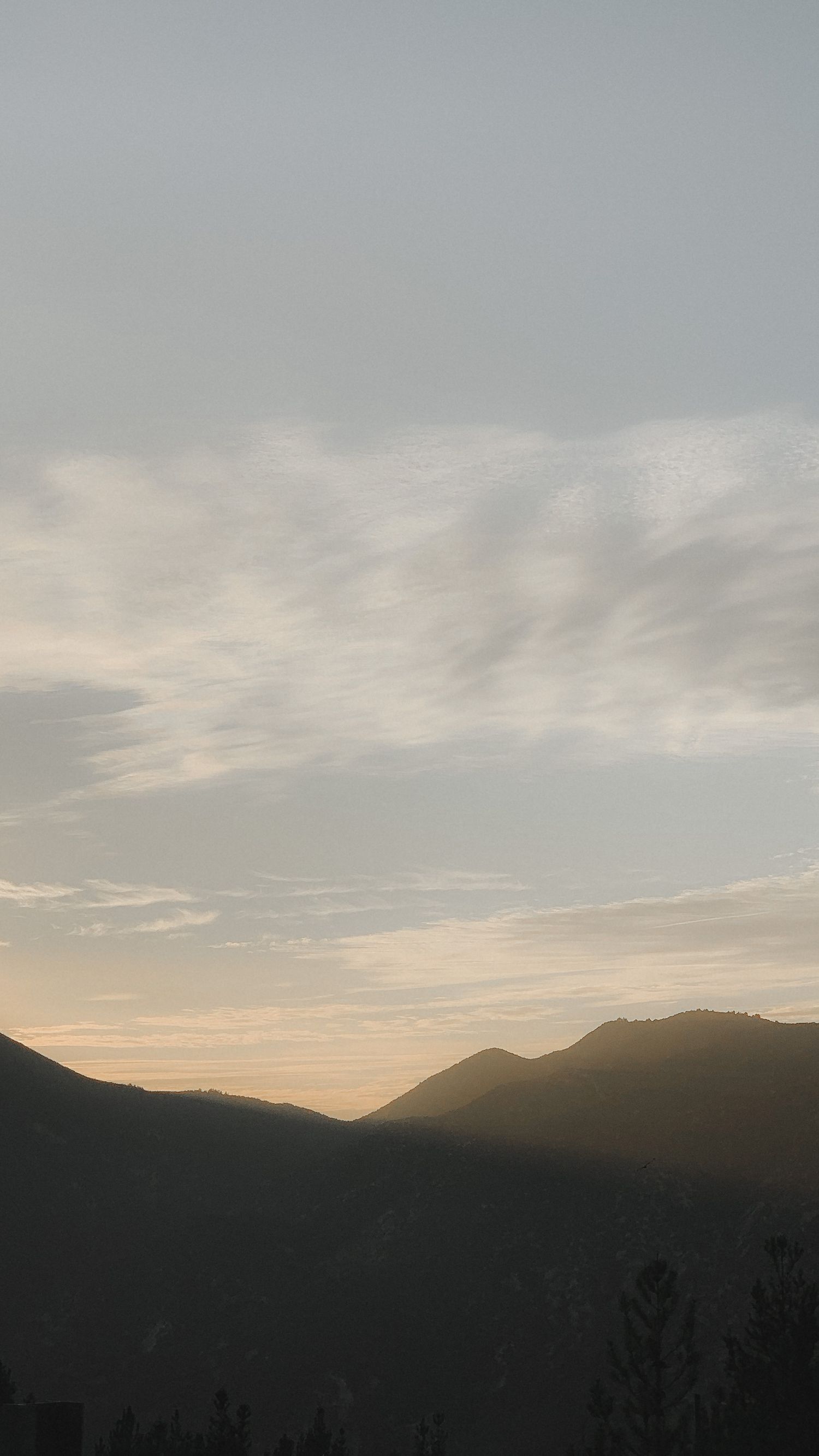 Moody sunset silhouette of mountain range under cloudy sky.