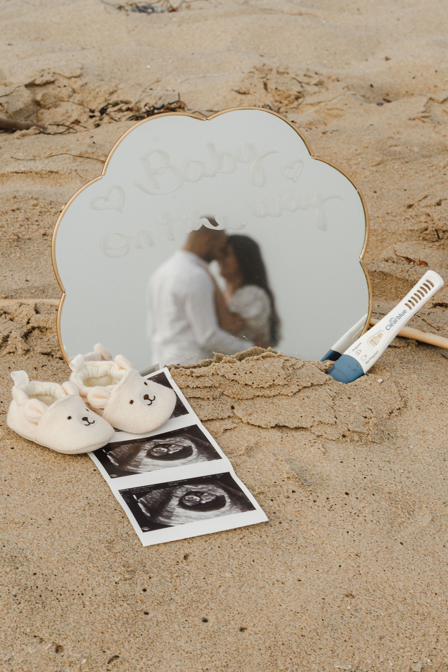 Wedding details arranged on beach sand with ultrasound photo and mirror.