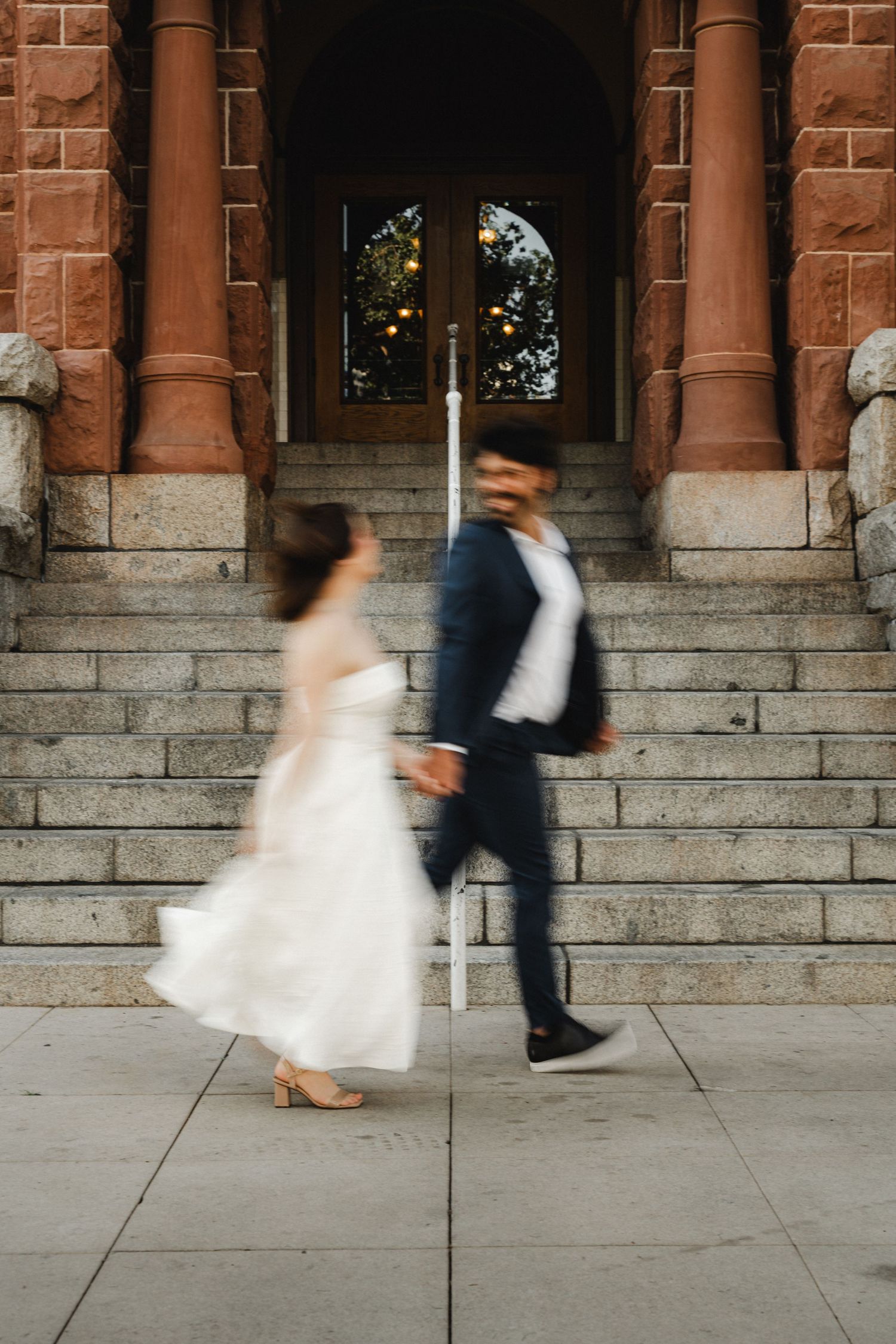 Motion blur captures couple running playfully on stone steps of historic building.