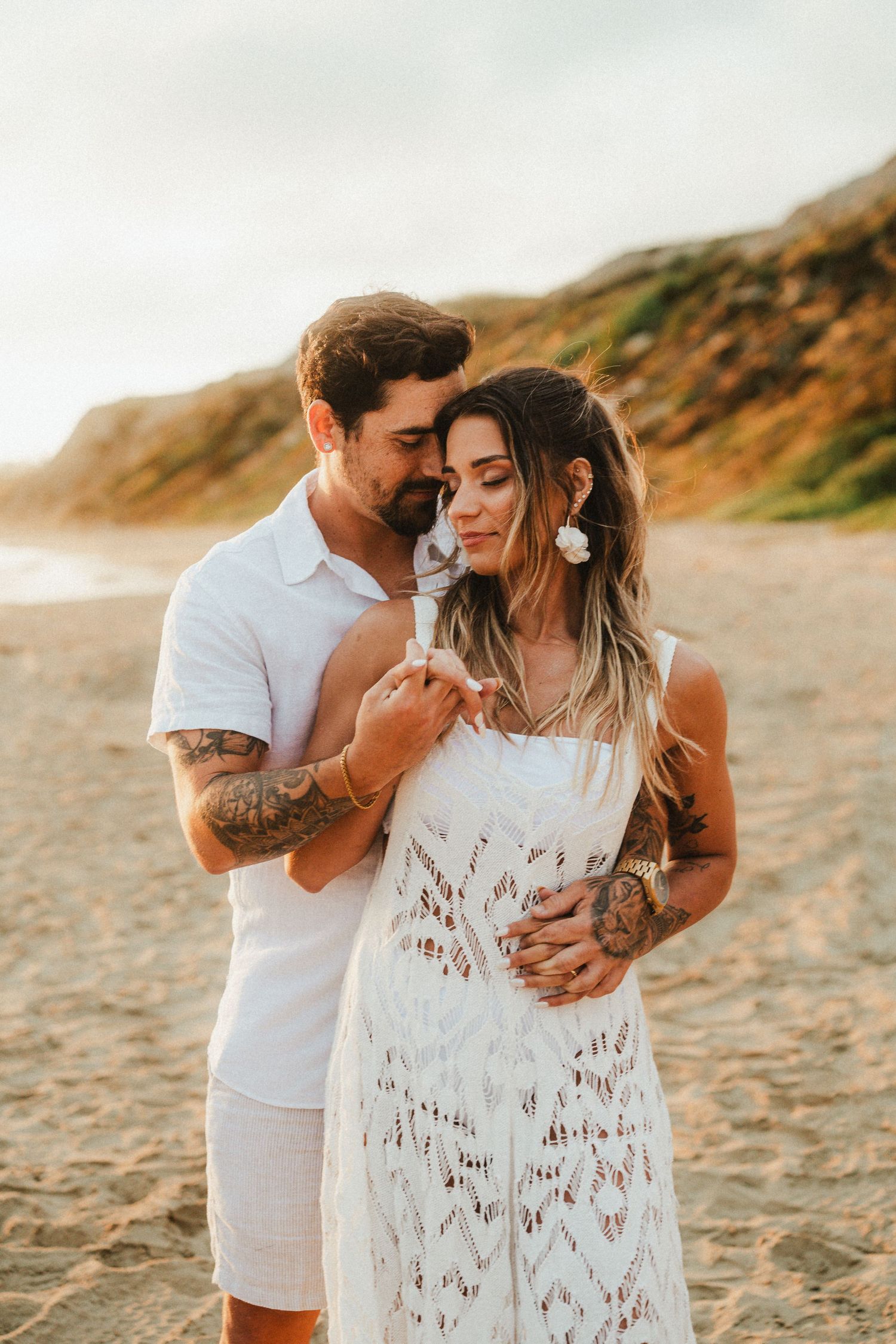 Romantic sunset beach photos of couple in white lace and casual attire.