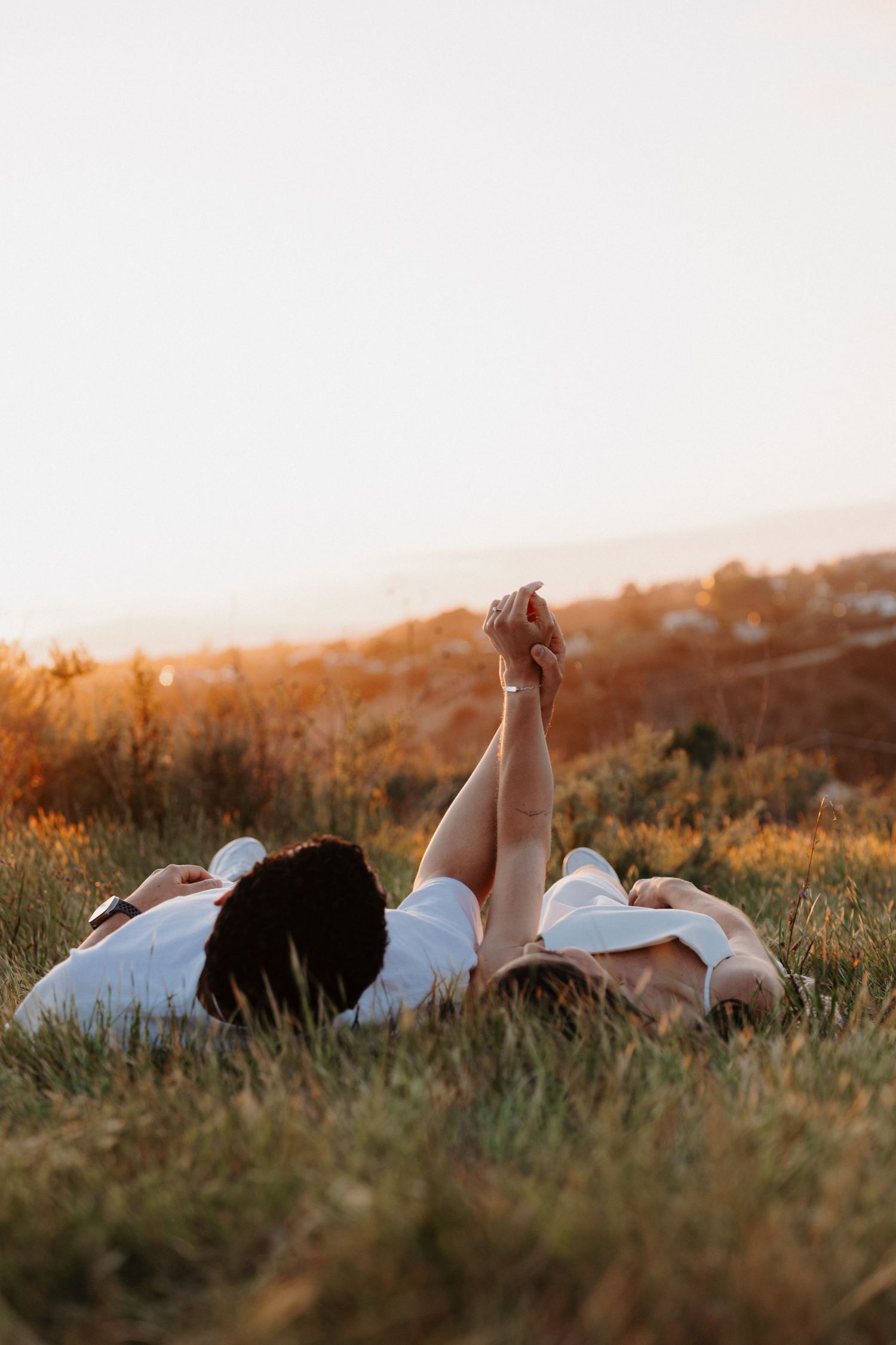 Couple lying in grass field during golden hour sunset.