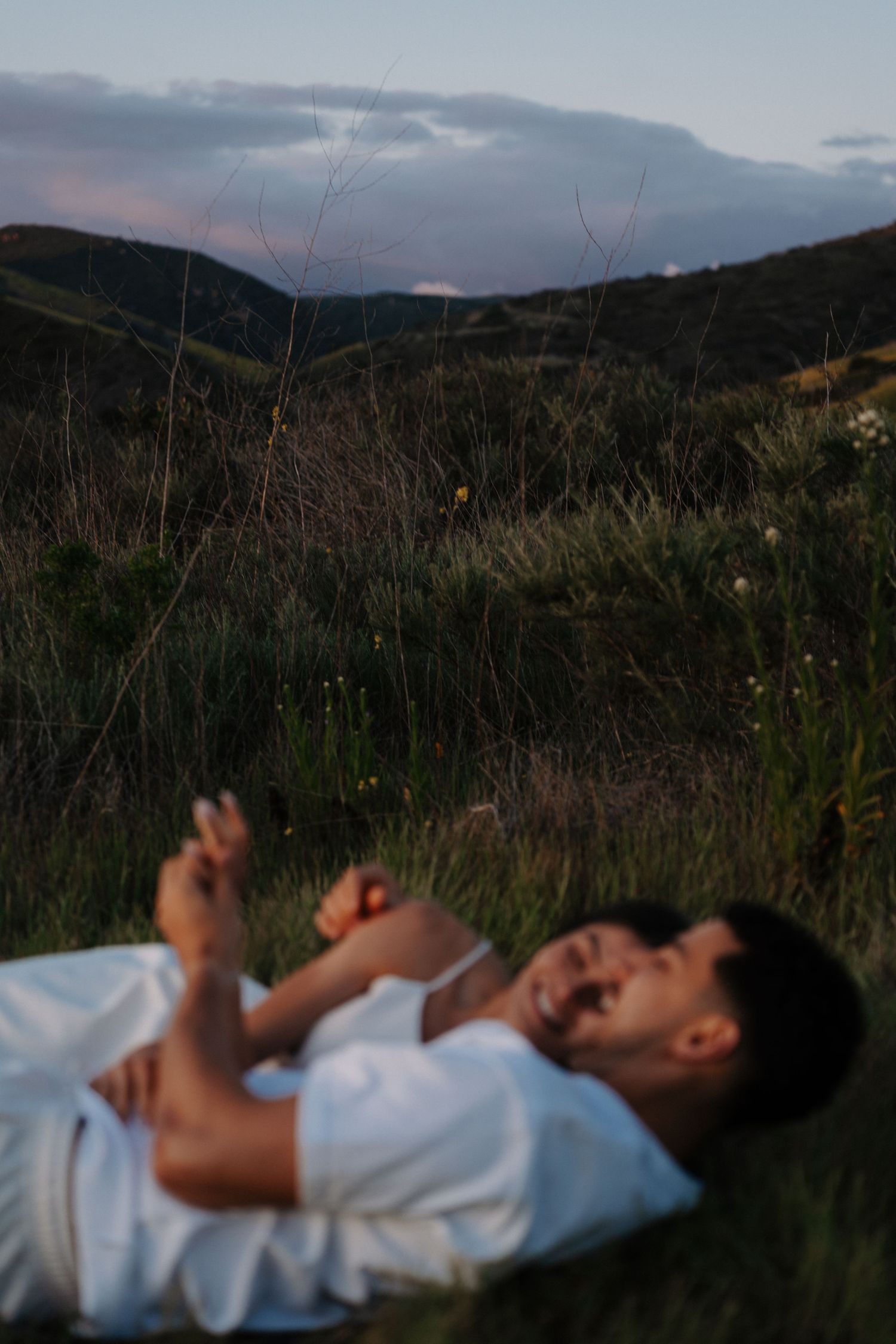 Person lying in mountain meadow at dusk with dramatic sky.