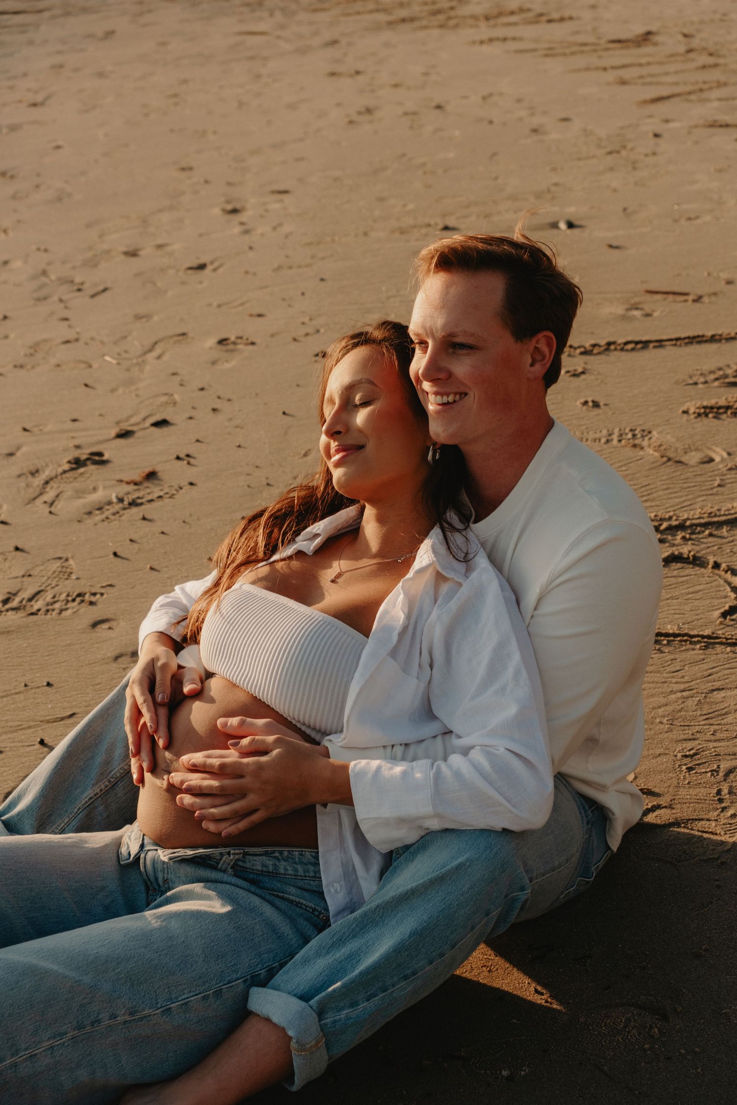 A couple shares an intimate moment while sitting together on the sandy beach at sunset.