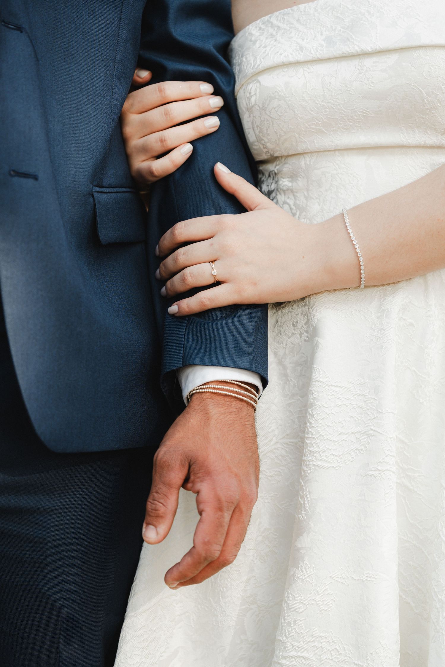 Detail shot of couple's hands and wedding attire showing white dress and navy suit.