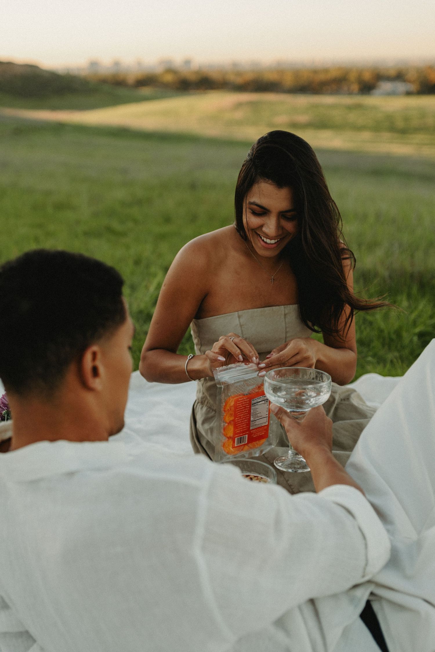 A couple enjoys an intimate outdoor dining experience in a grassy field during golden hour.